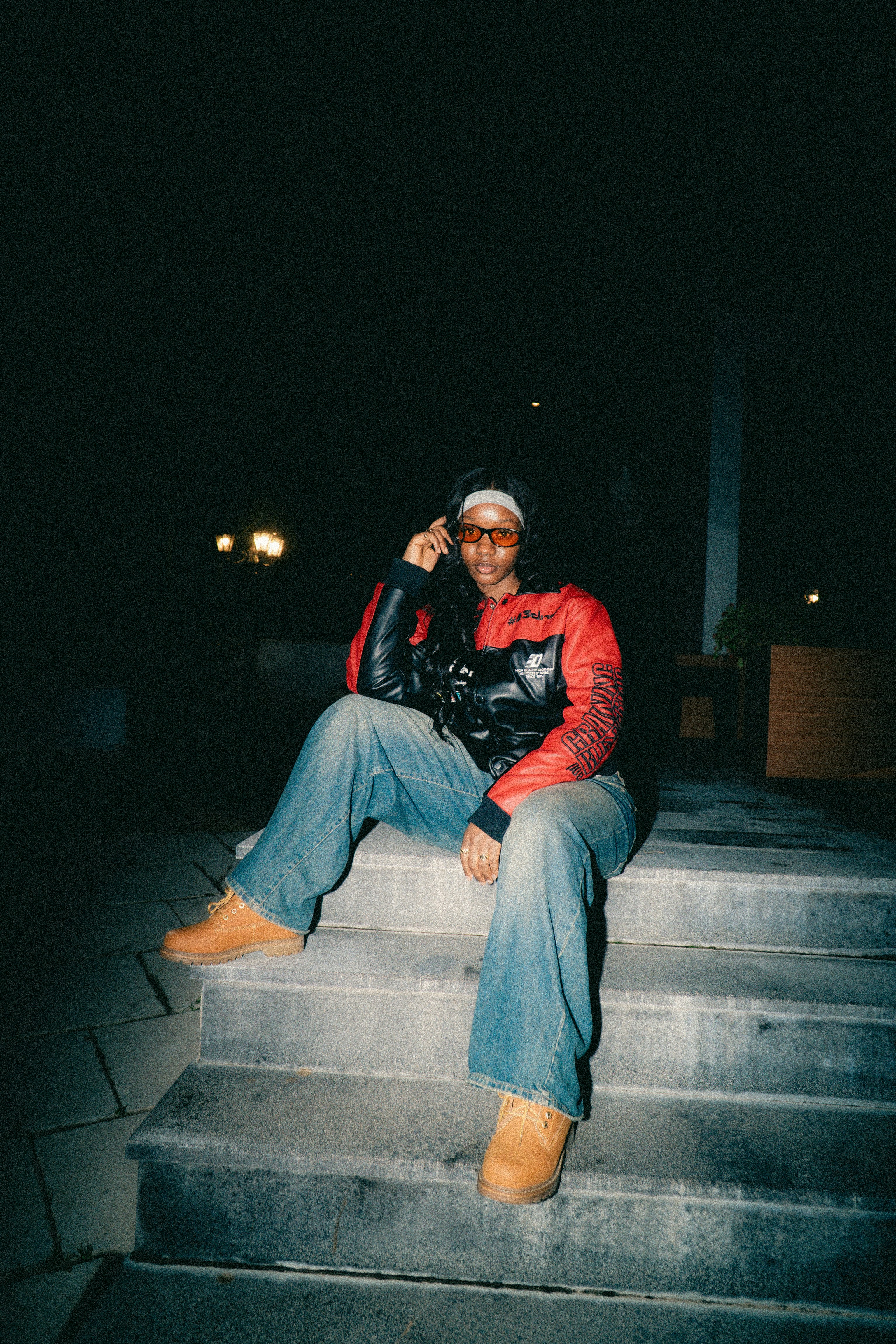 Woman in red jacket and jeans sits on steps.
