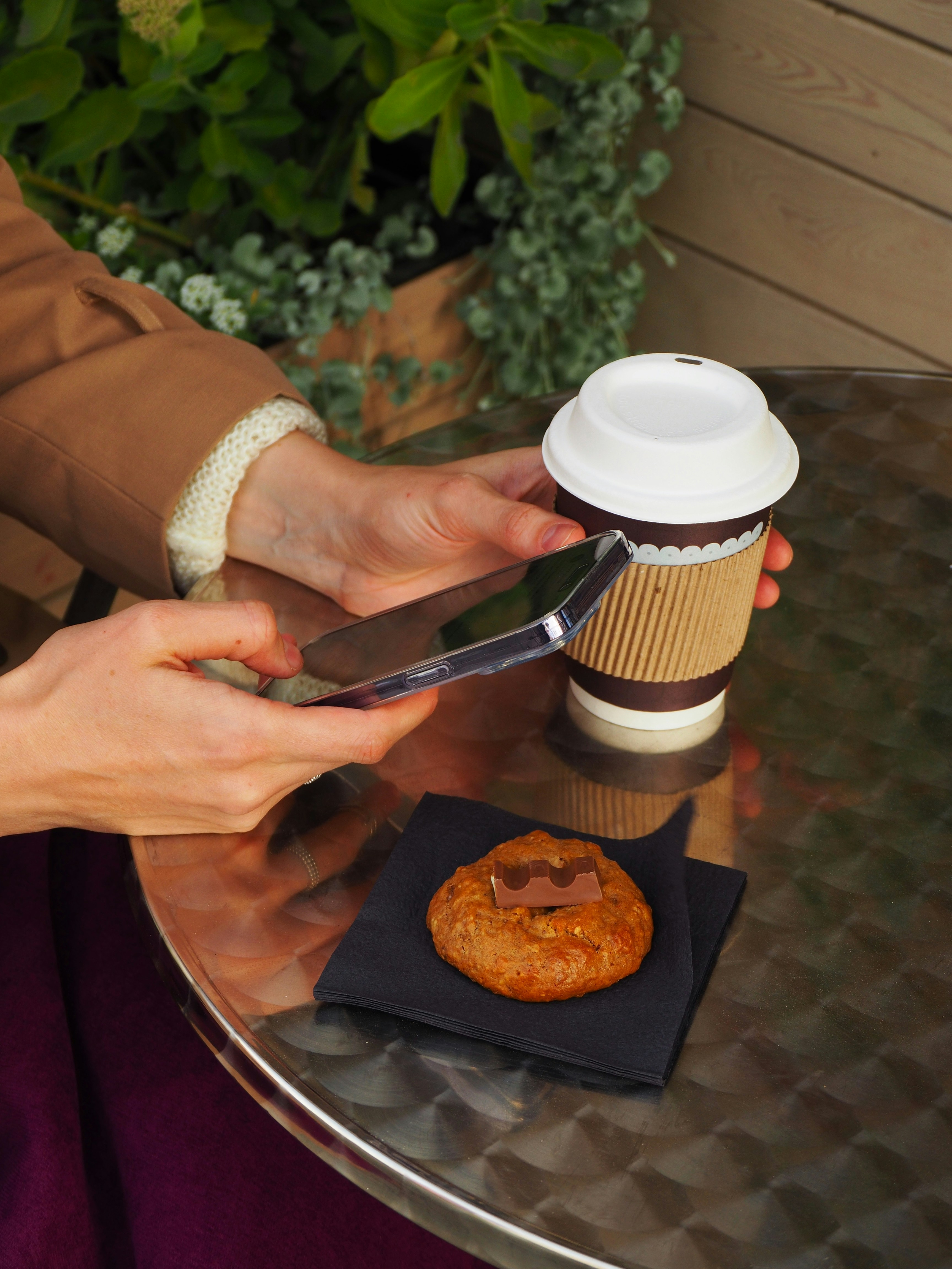 Person, die das Handy mit Kaffee und Gebäck auf dem Tisch benutzt