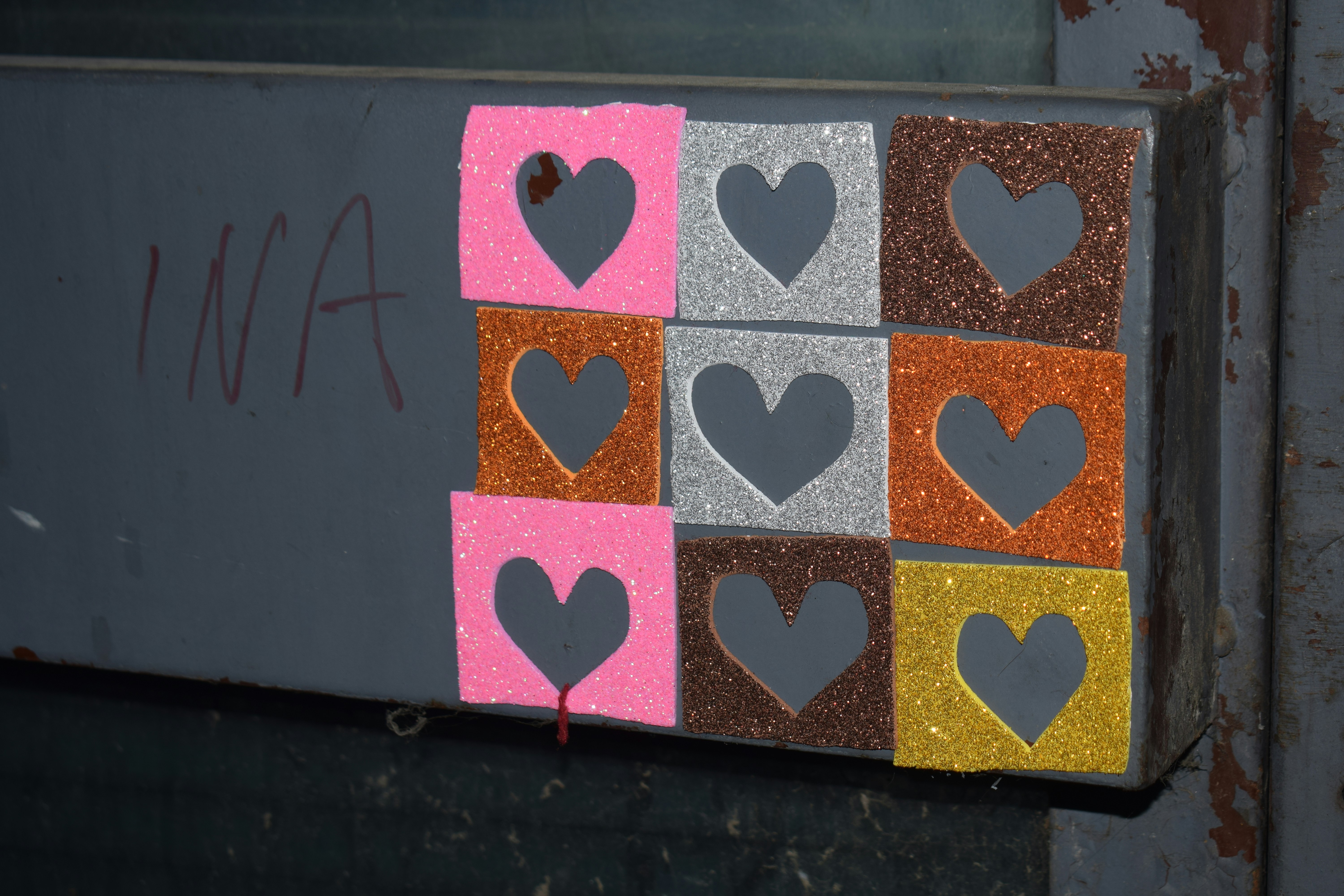 Nine glitter squares with heart cutouts arranged on a surface.