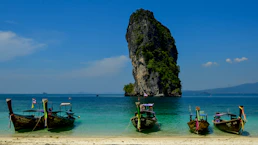 Longtail boats anchored near a rocky island in the ocean.