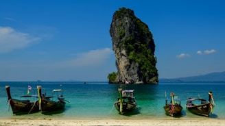 Longtail boats anchored near a rocky island in the ocean.