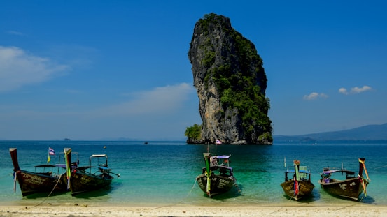 Longtail boats anchored near a rocky island in the ocean.