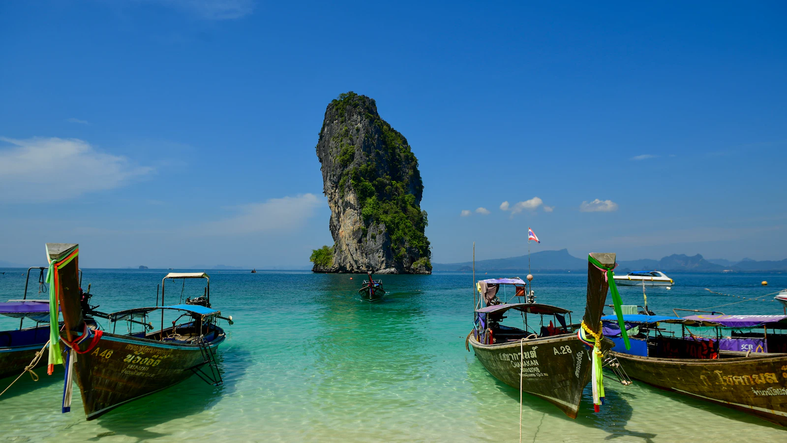 Colourful longtail boats anchored in clear water near a limestone island in southern Thailand on a sunny day