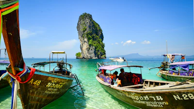 Longtail boats float in clear turquoise water near island.