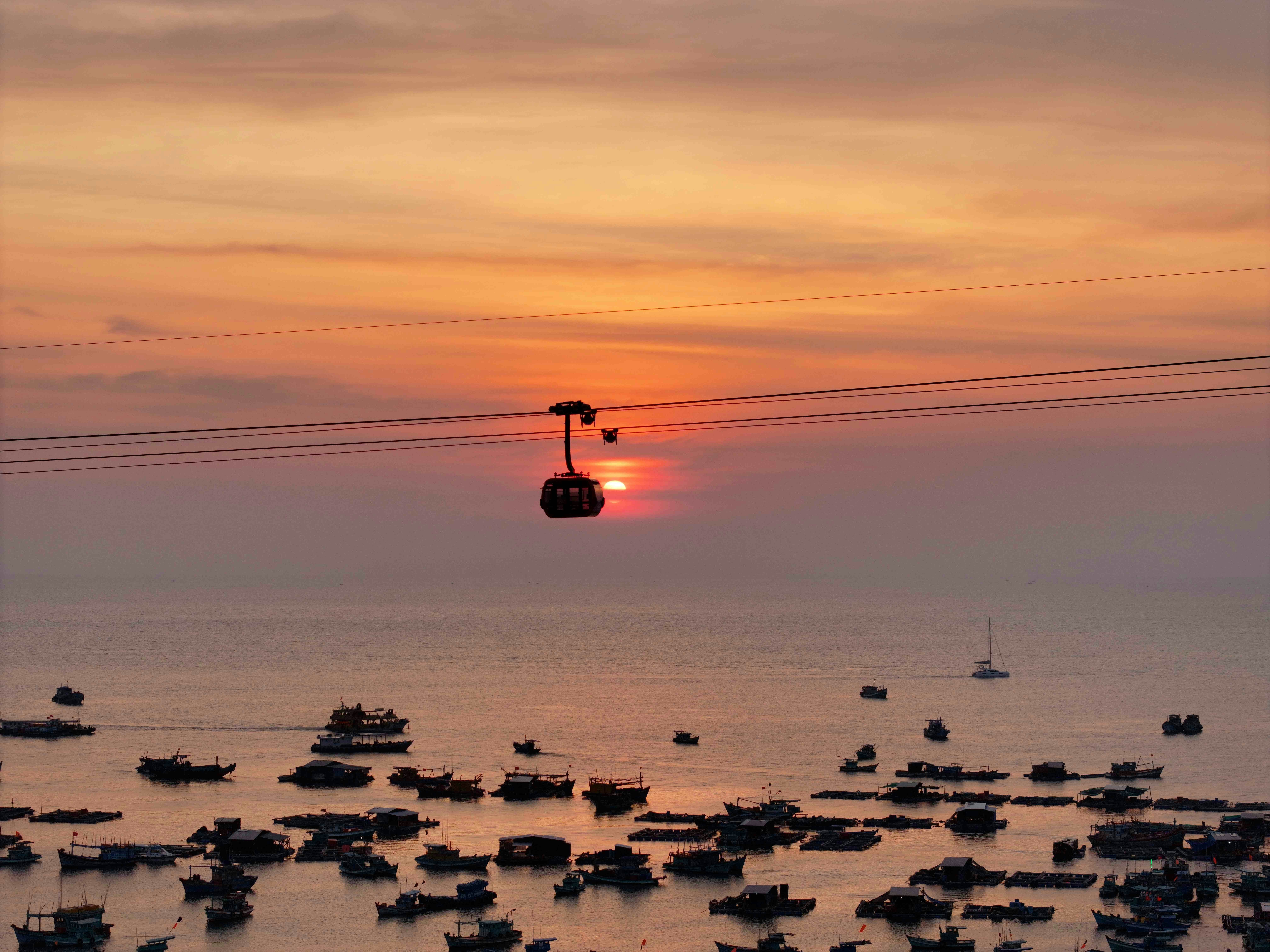 Cable car crossing the ocean at sunset with boats.