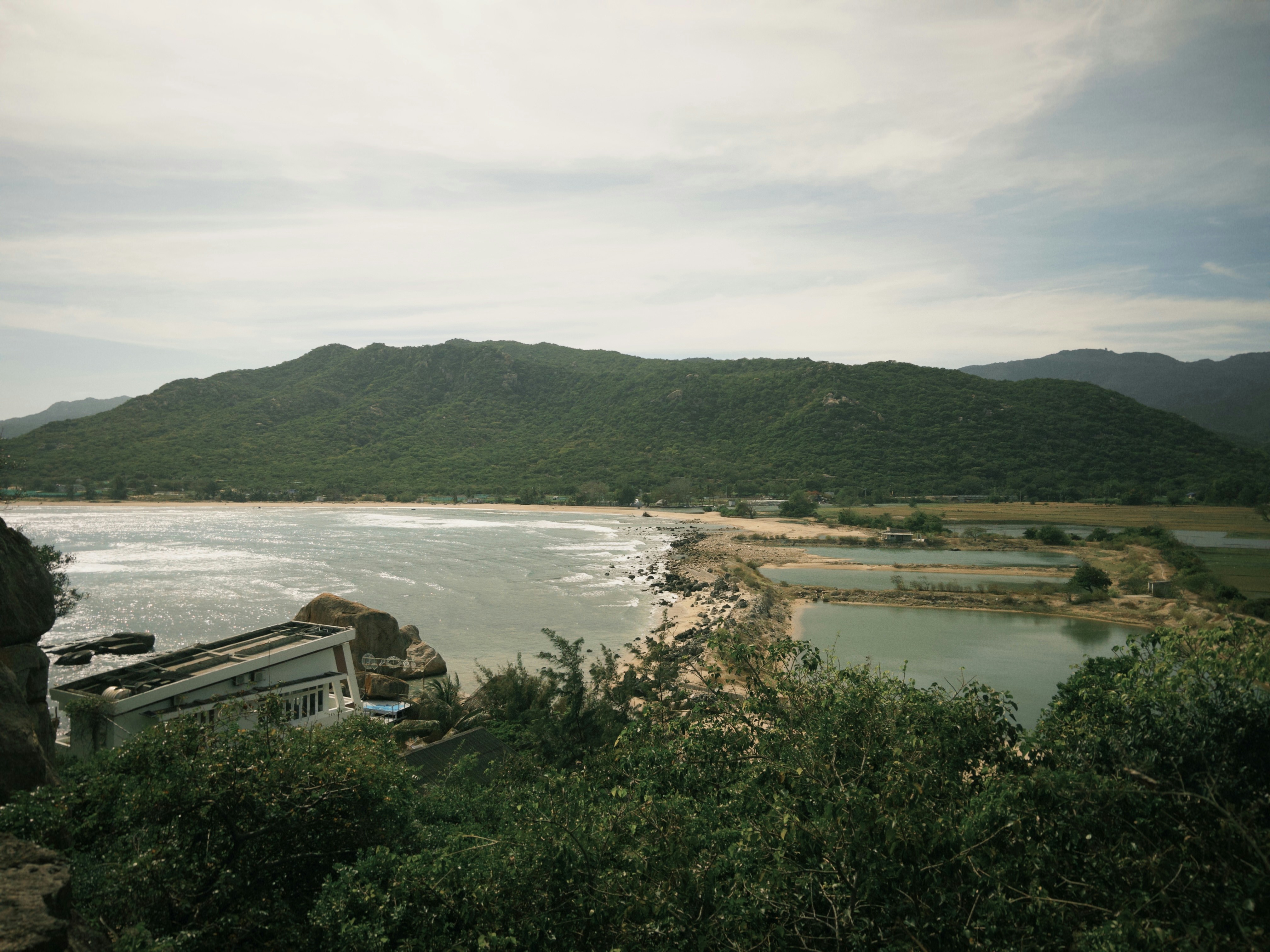 Green hills overlook a tranquil coastal landscape with calm waters.
