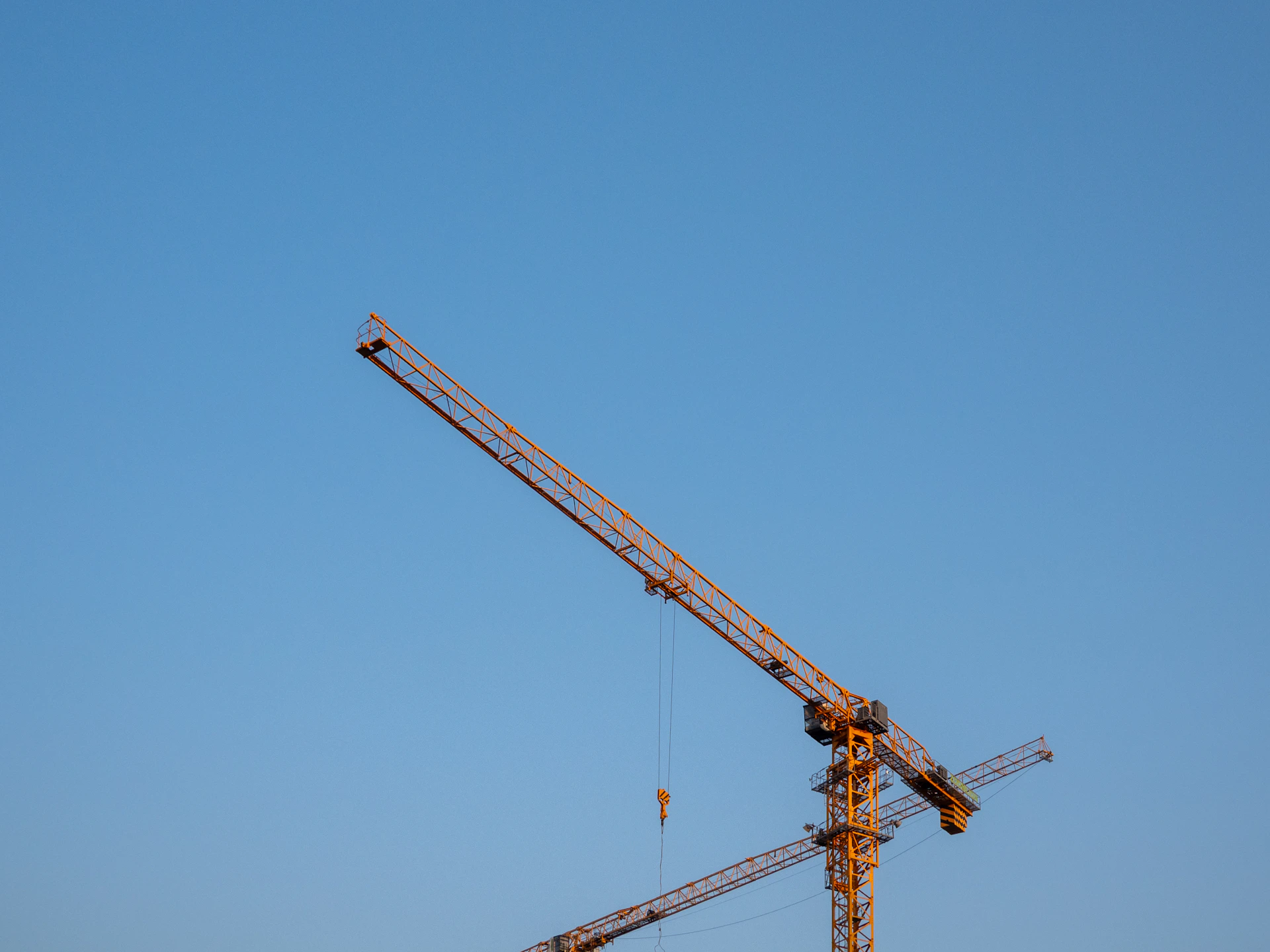 Two construction cranes against a clear blue sky