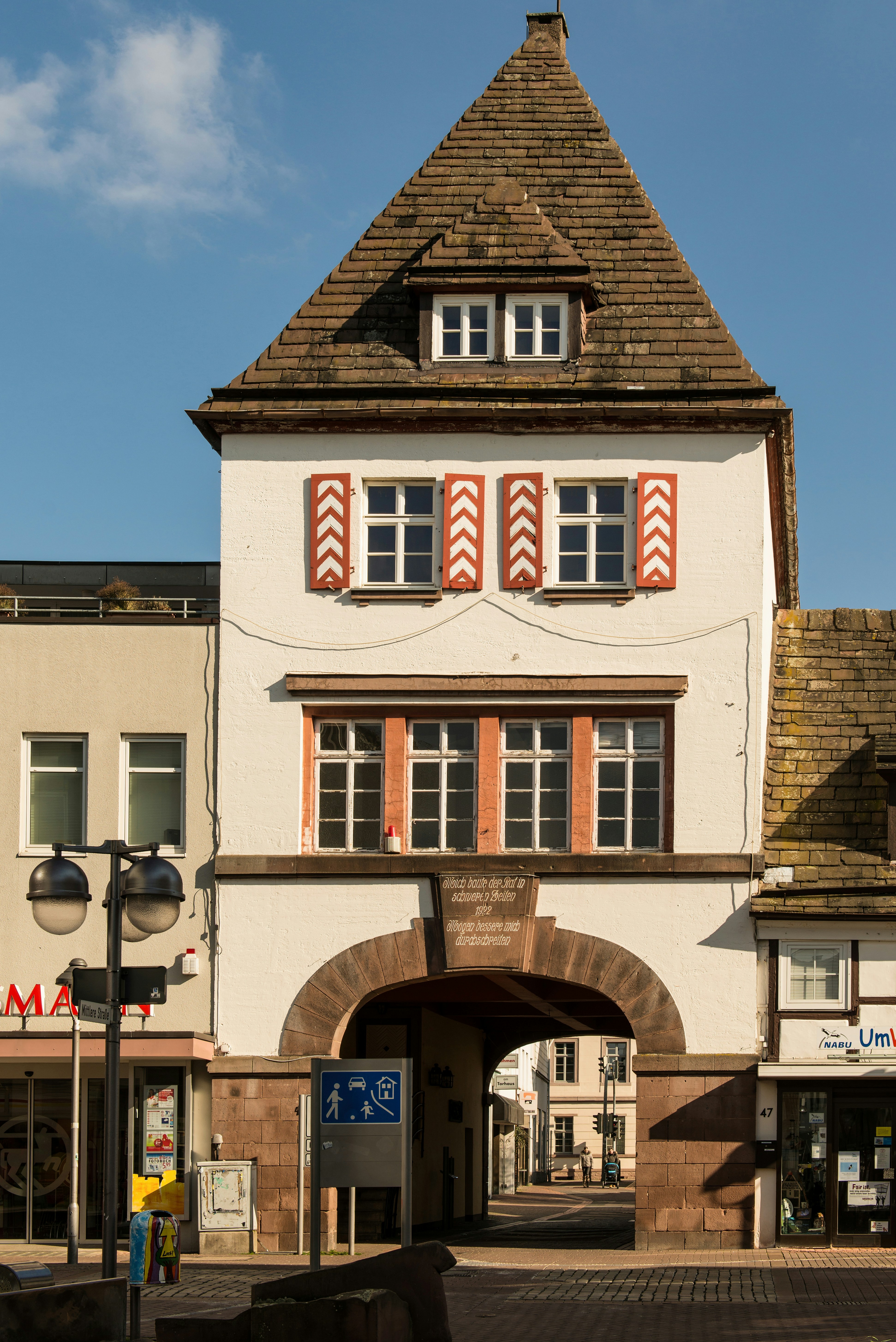 Historic stone archway with white building and red shutters