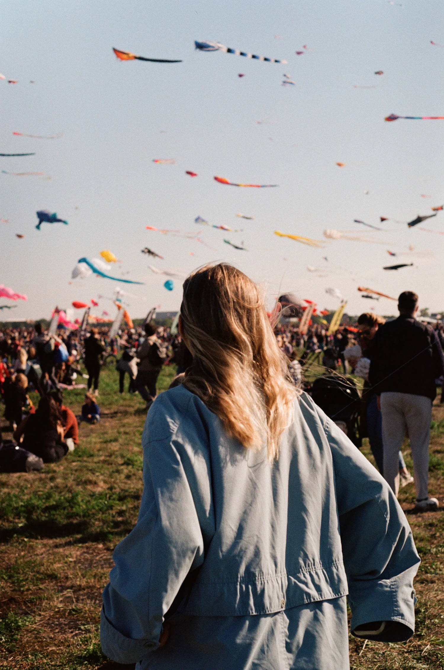 A woman on a crowded kite field watching dozens of kites in the sky
