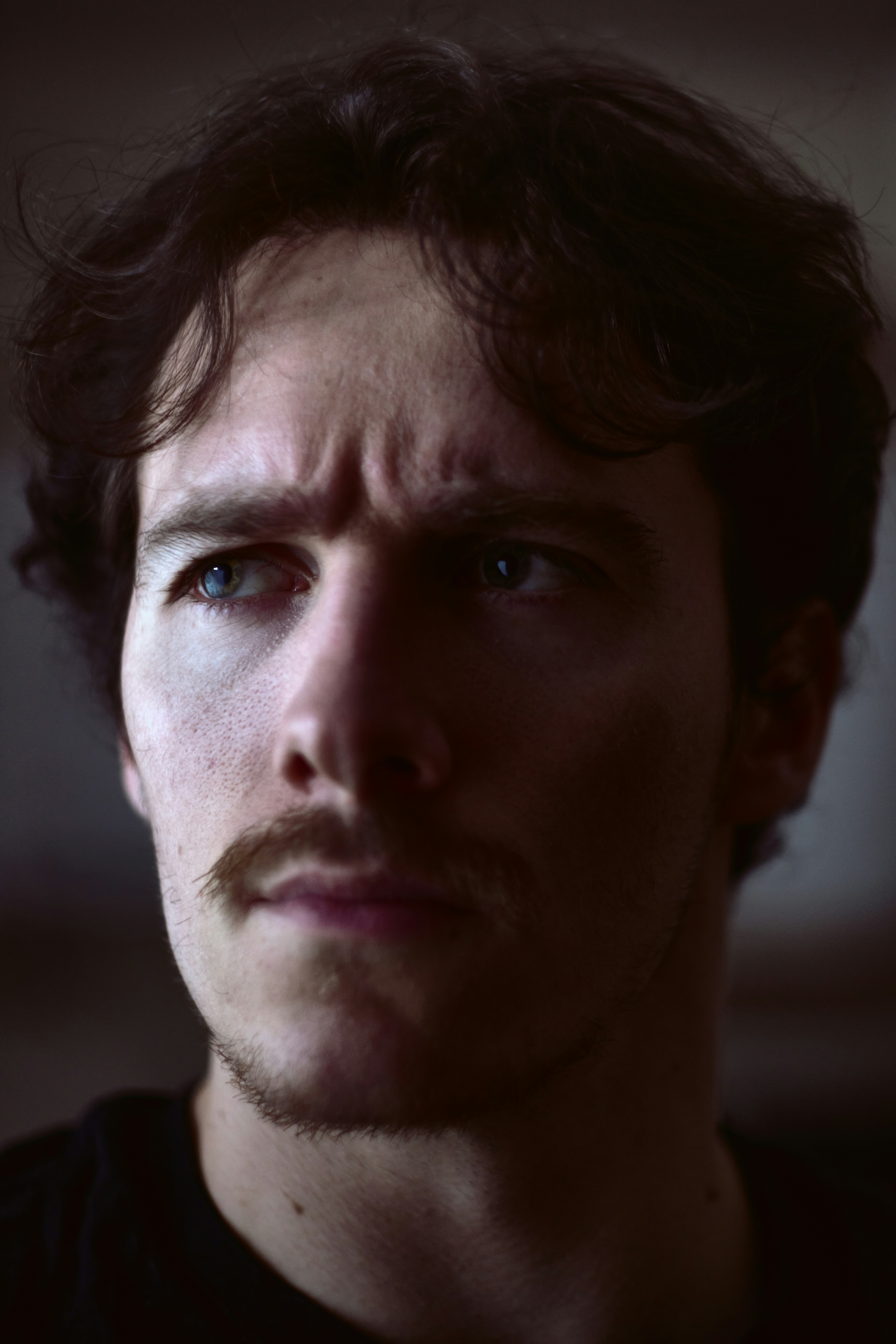 A man with a mustache looks thoughtfully to the side.