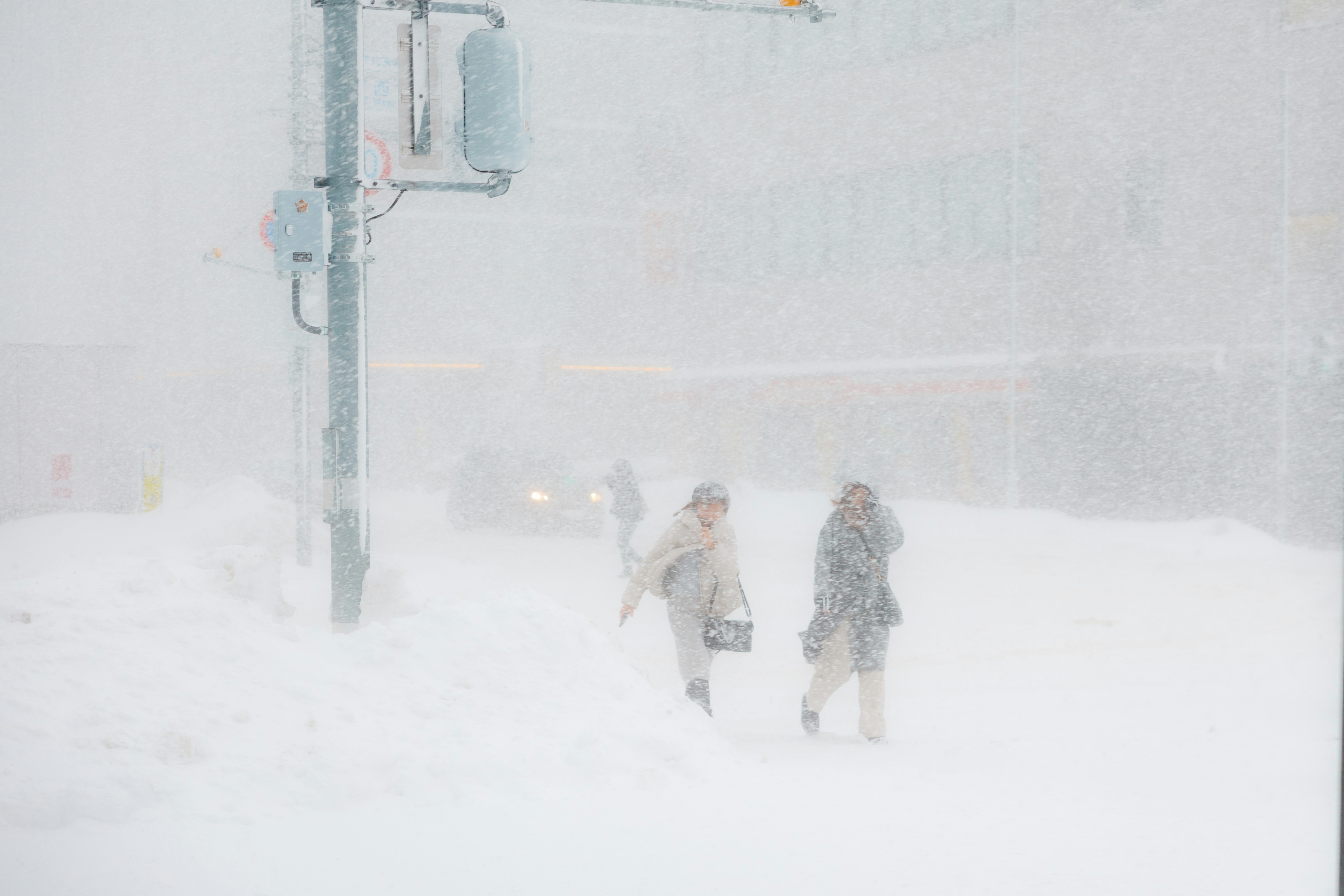 Two people walk through a blizzard on a city street.