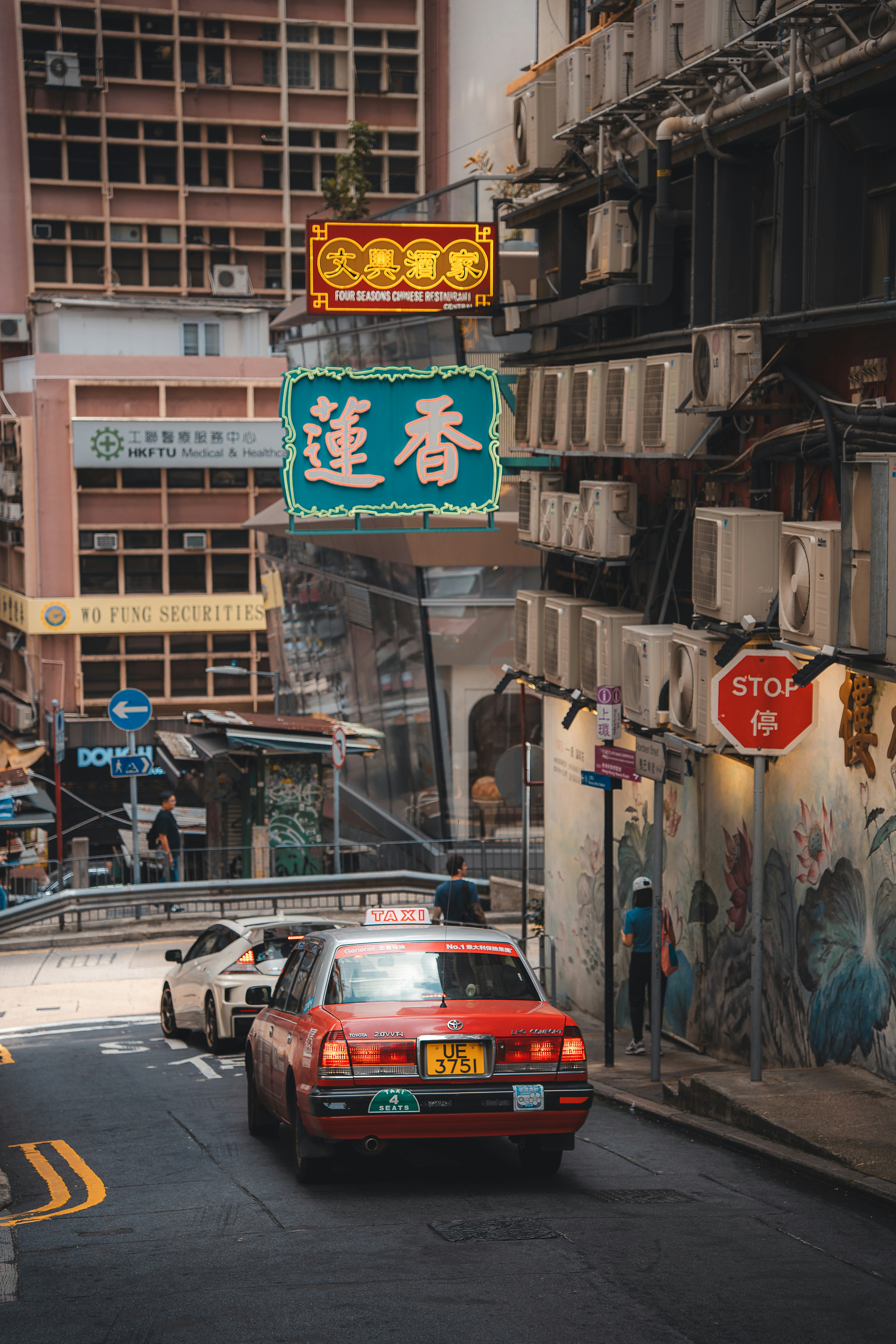 Red car driving up a steep city street.