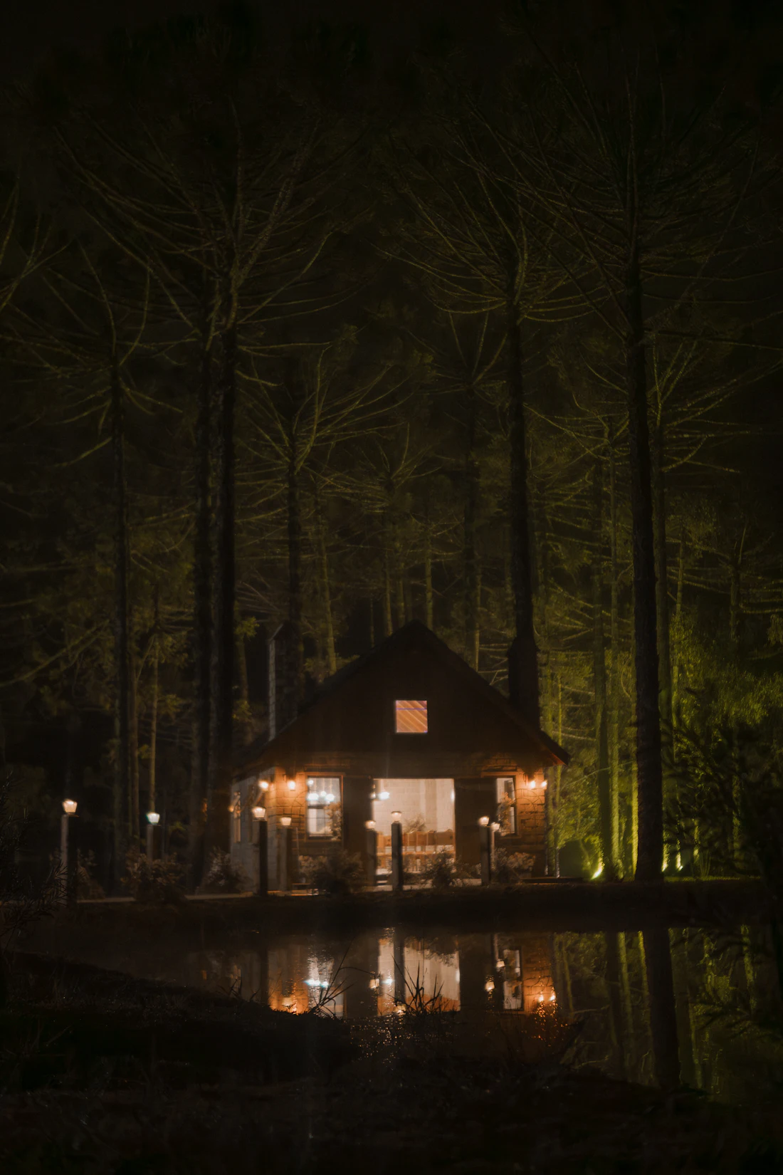 Cabaña iluminada de noche, reflejada en el agua