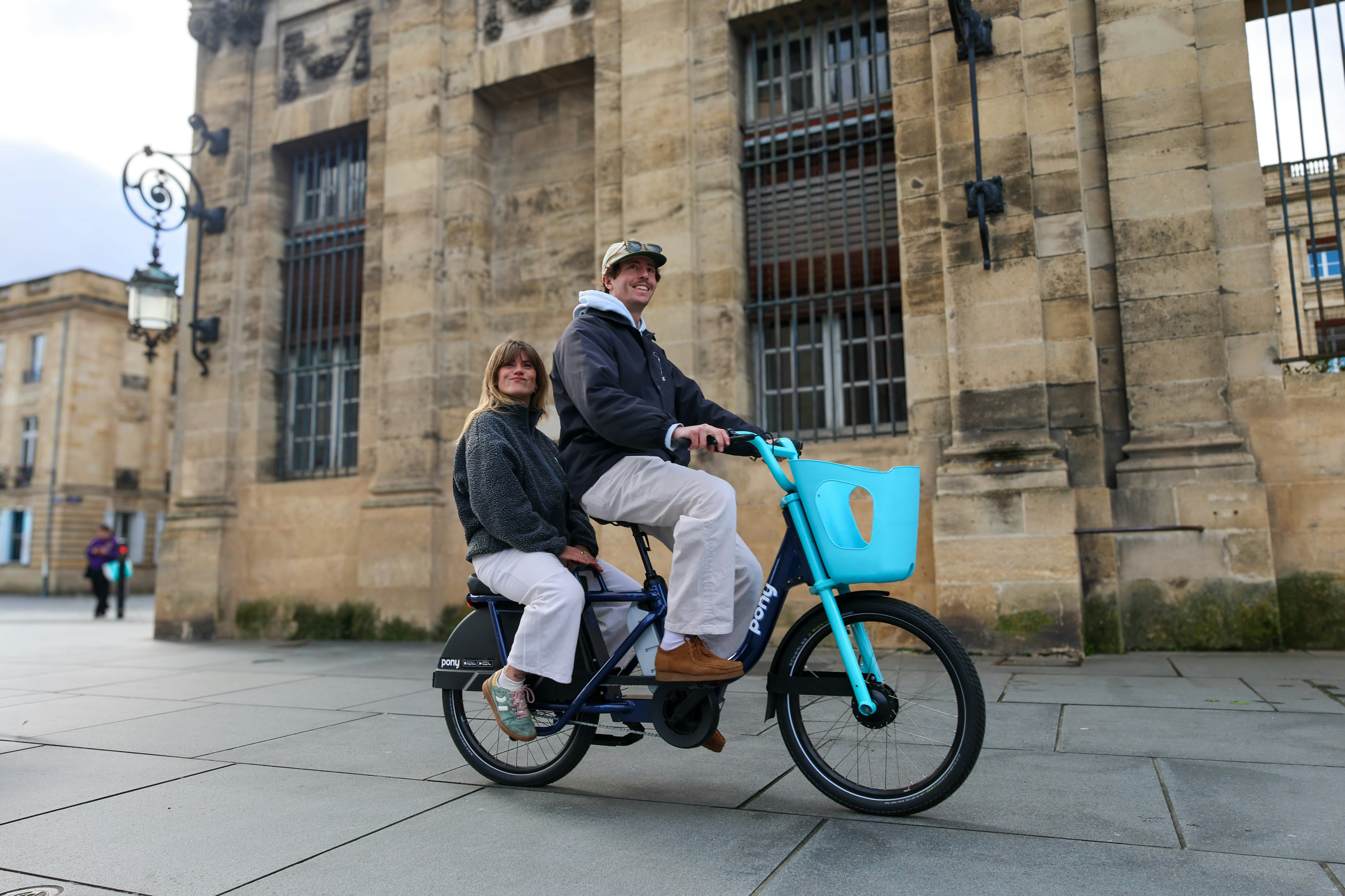 Couple riding a bicycle in front of a stone building.