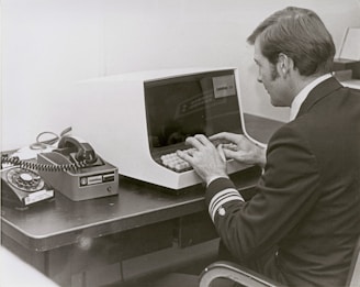 Man in uniform types on vintage computer terminal.