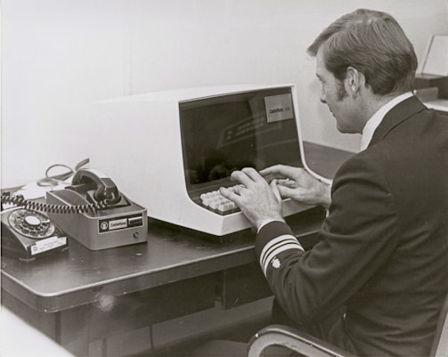 Man in uniform types on vintage computer terminal.