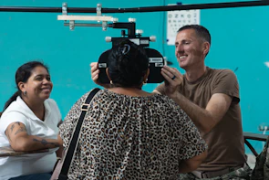Optometrist examines patient's eyes with equipment.