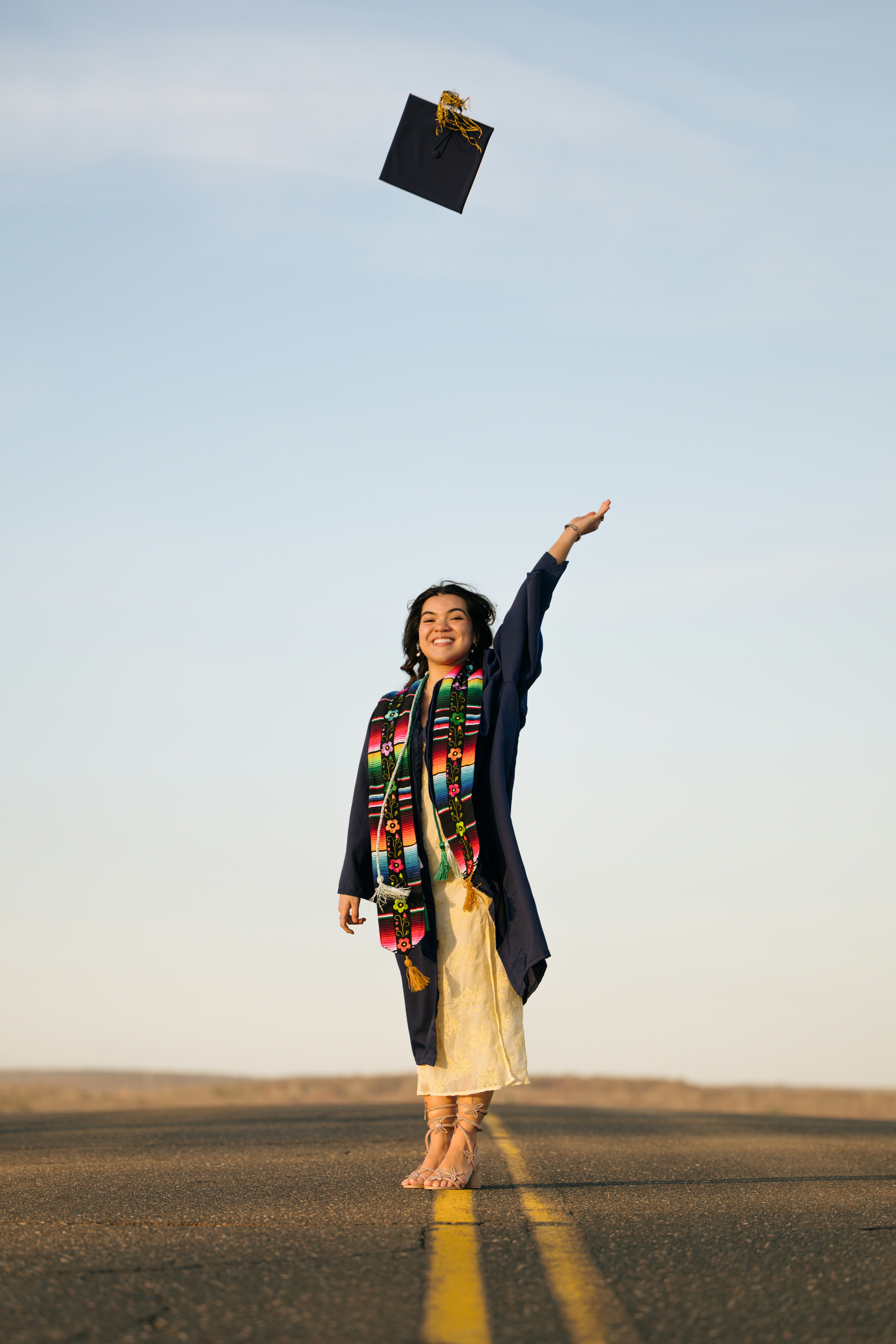 A graduate throws cap in the air on a road.