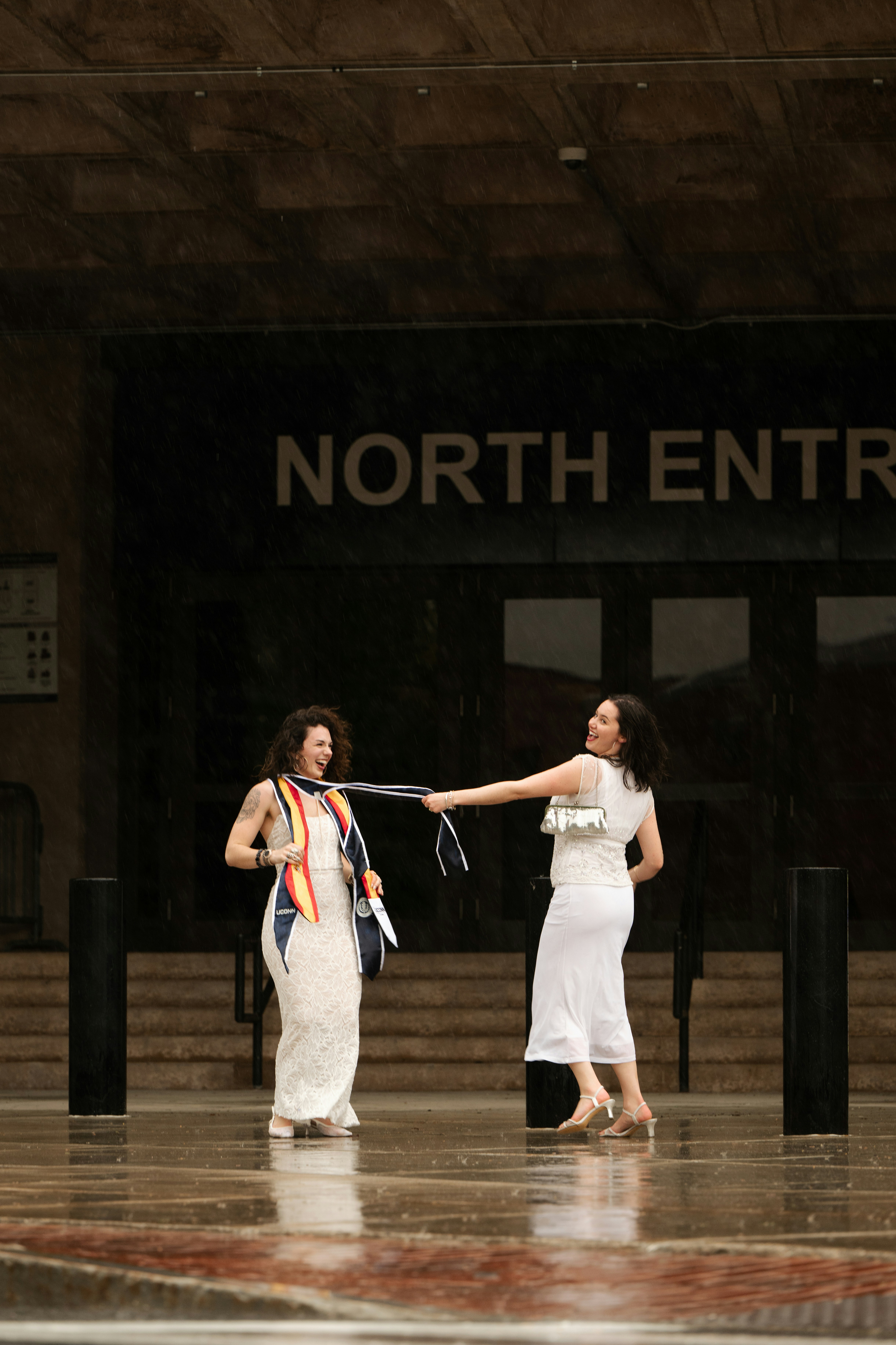 Two women in white outfits pulling a rope outside.