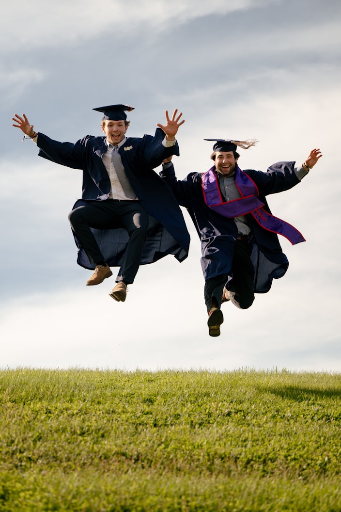 Two graduates in caps and gowns jumping in the air