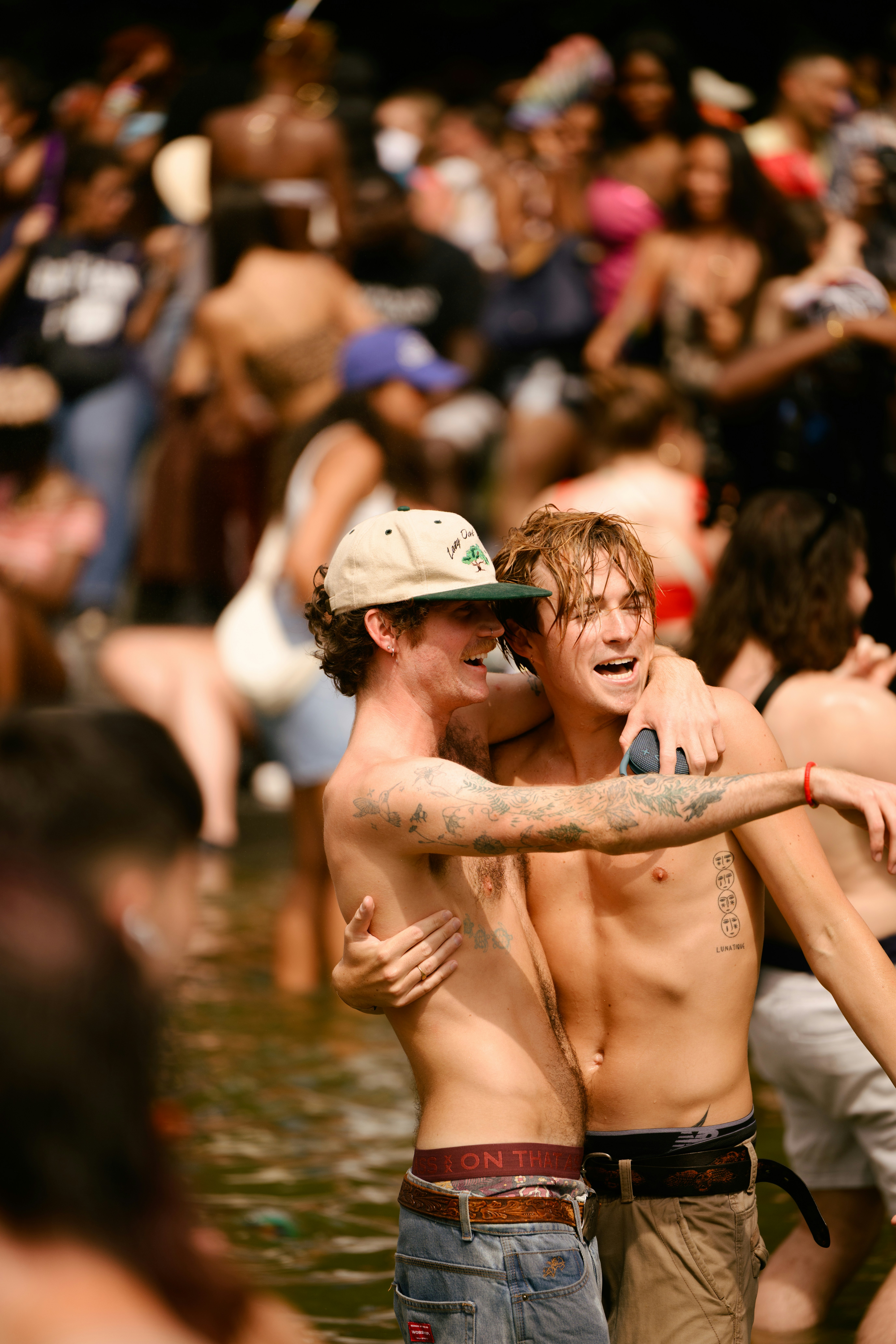 Two young men hug in a crowded outdoor gathering.
