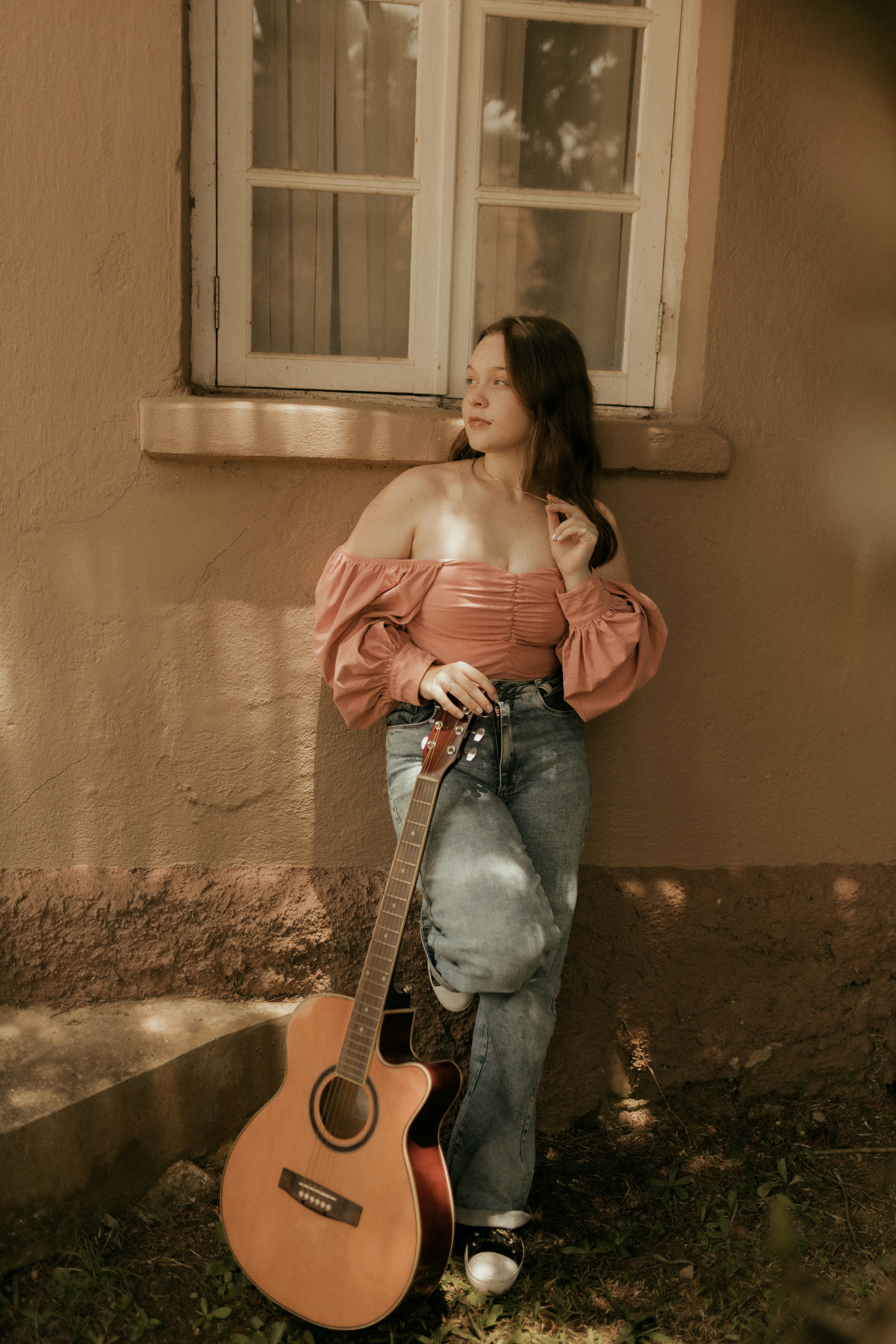 Young woman with guitar leaning against wall