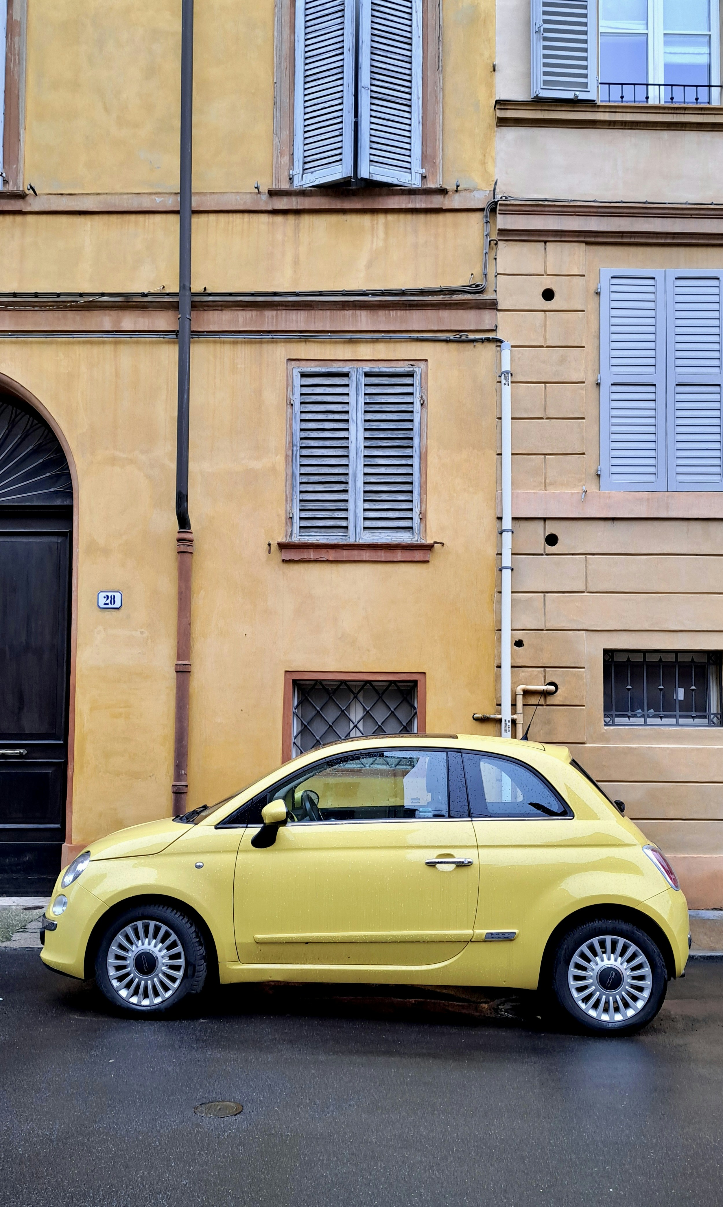 A yellow fiat 500 parked on a wet street.