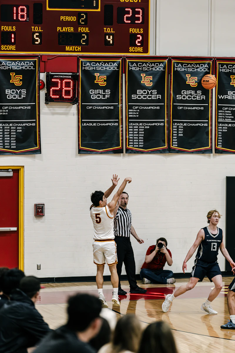 Basketball player shoots ball near referee and spectators