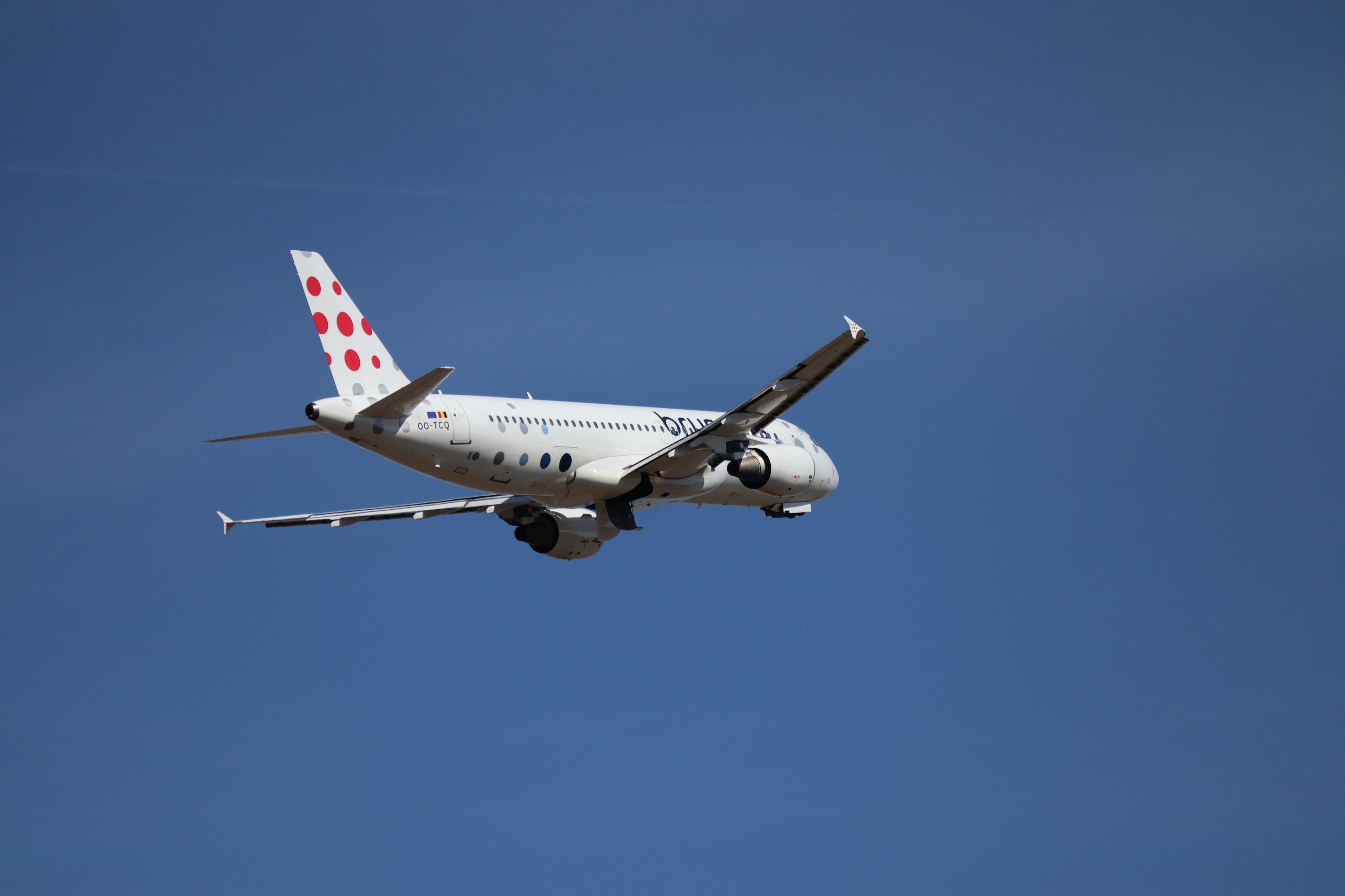 Ein weißes Flugzeug mit roten Punkten fliegt am Himmel.