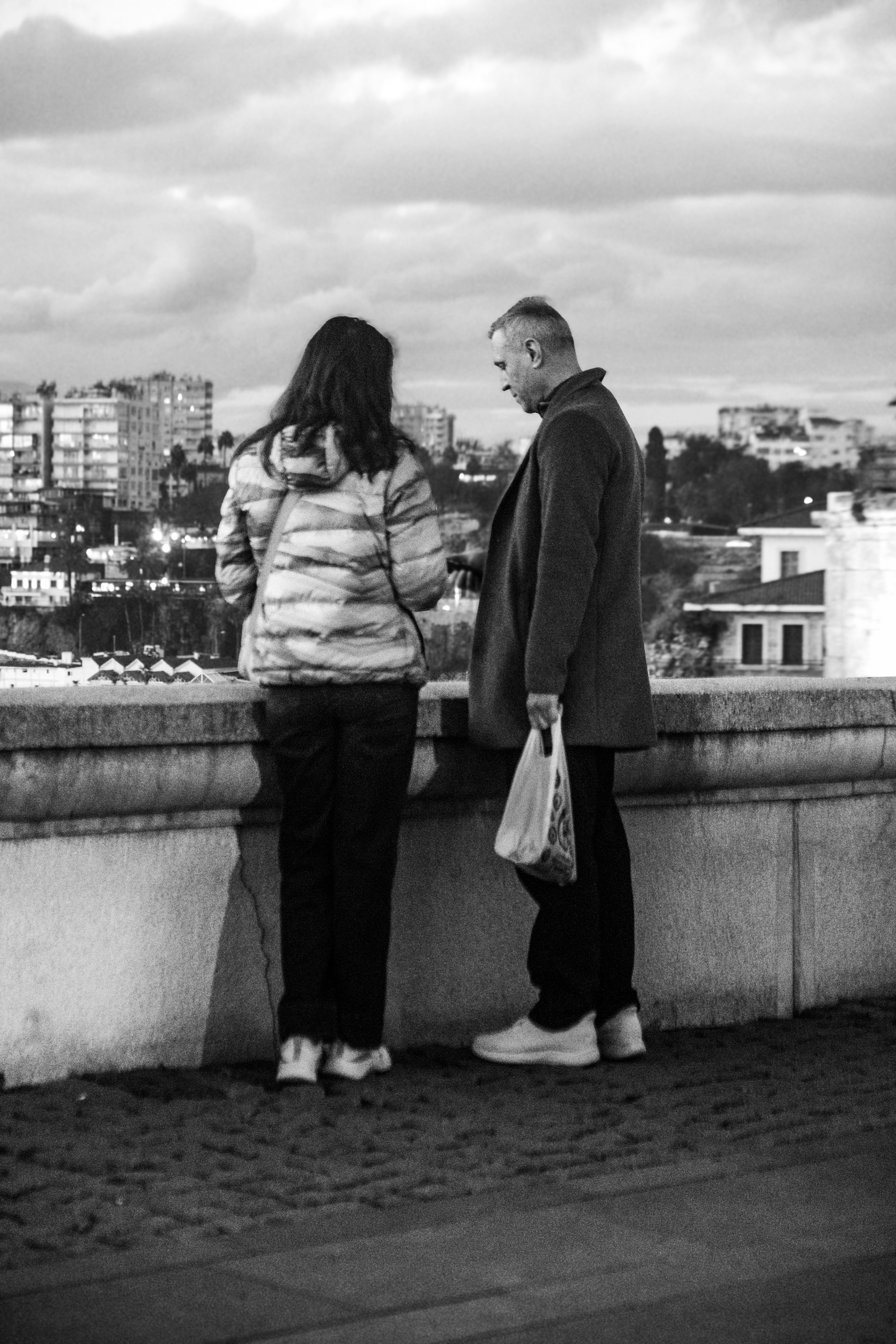 Duas pessoas em pé em uma varanda com vista para prédios da cidade.