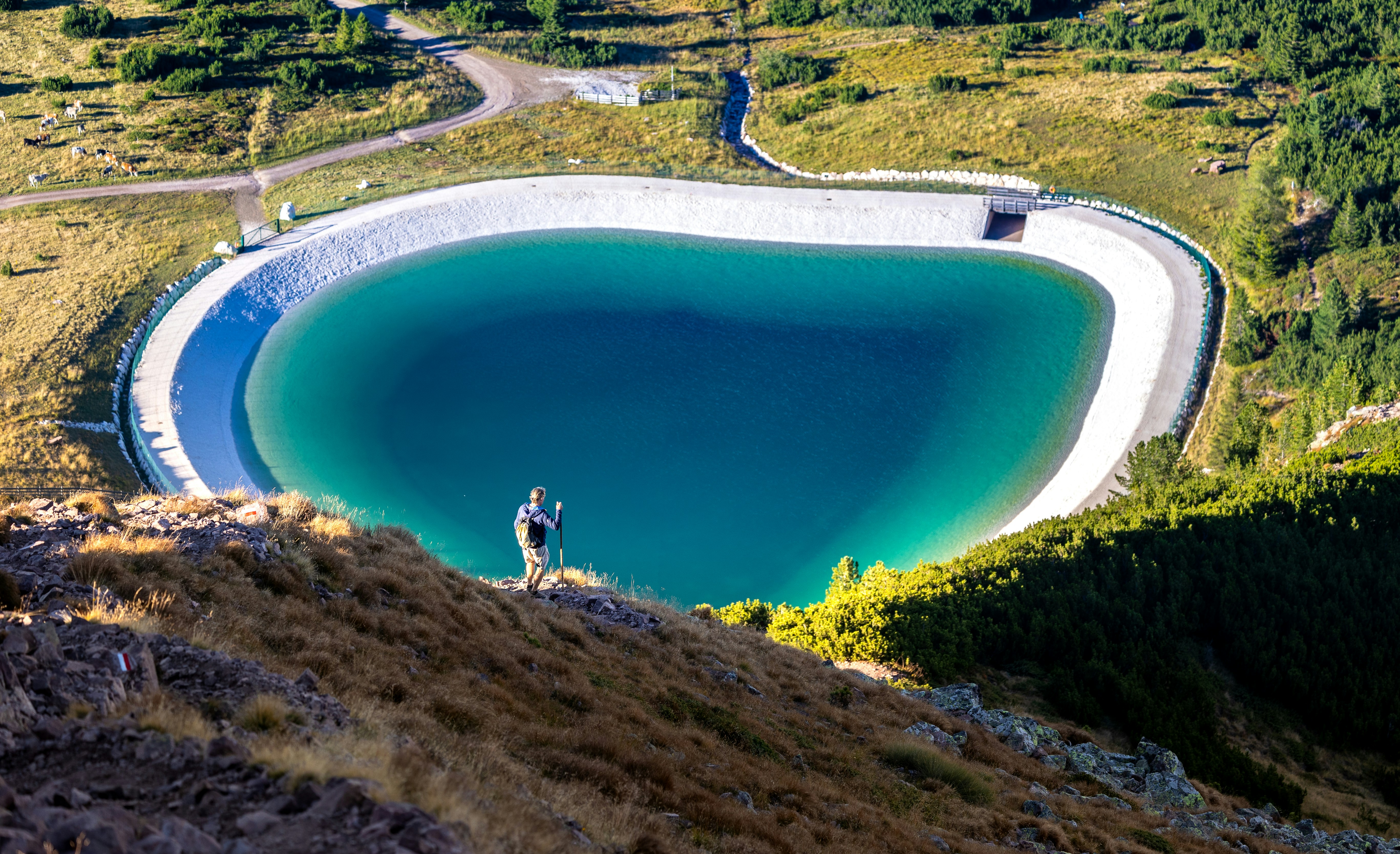A person stands by a large reservoir in the mountains.