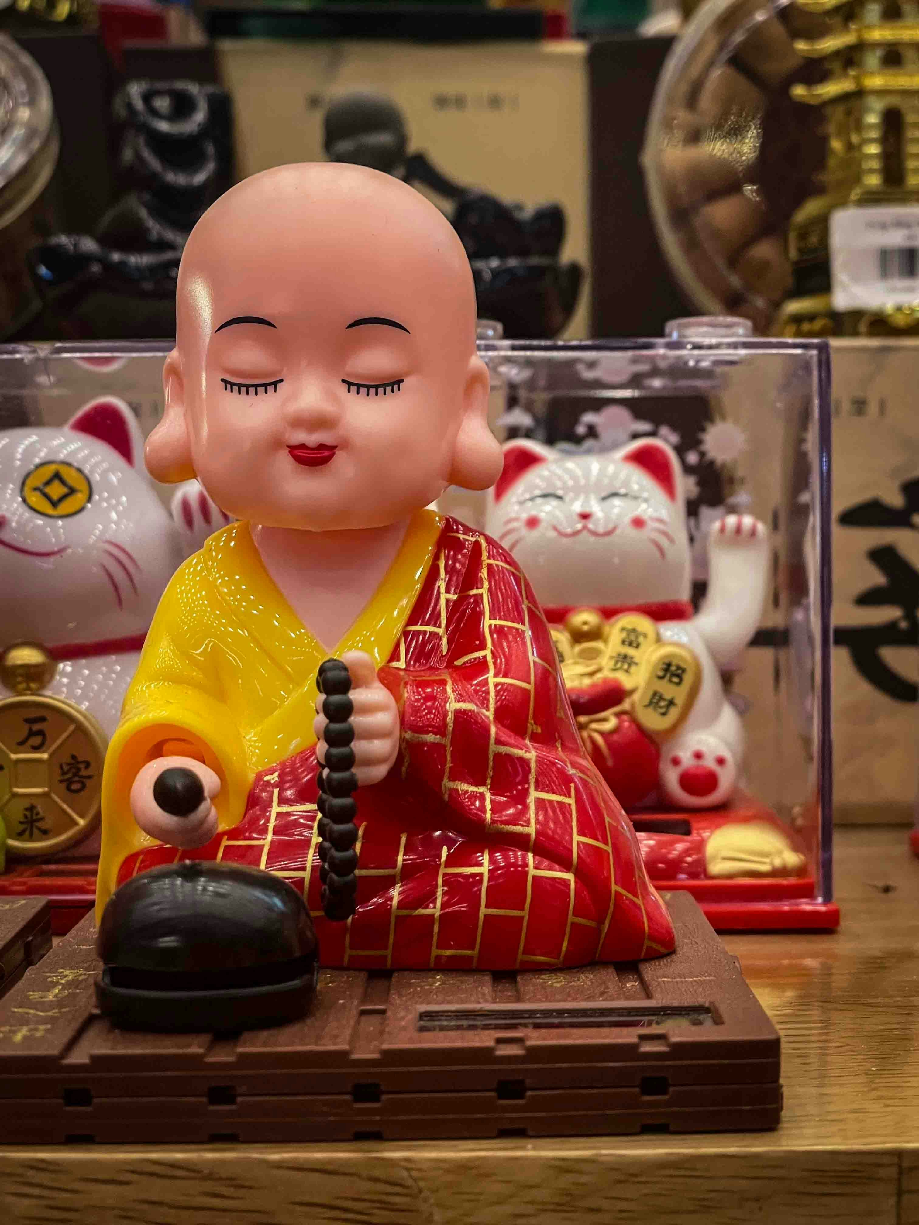 A small monk figurine holding prayer beads with cats behind.