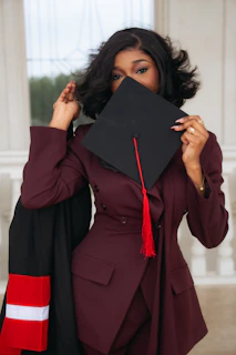 Woman in graduation attire holding cap over her face