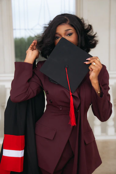 Woman in graduation attire holding cap over her face