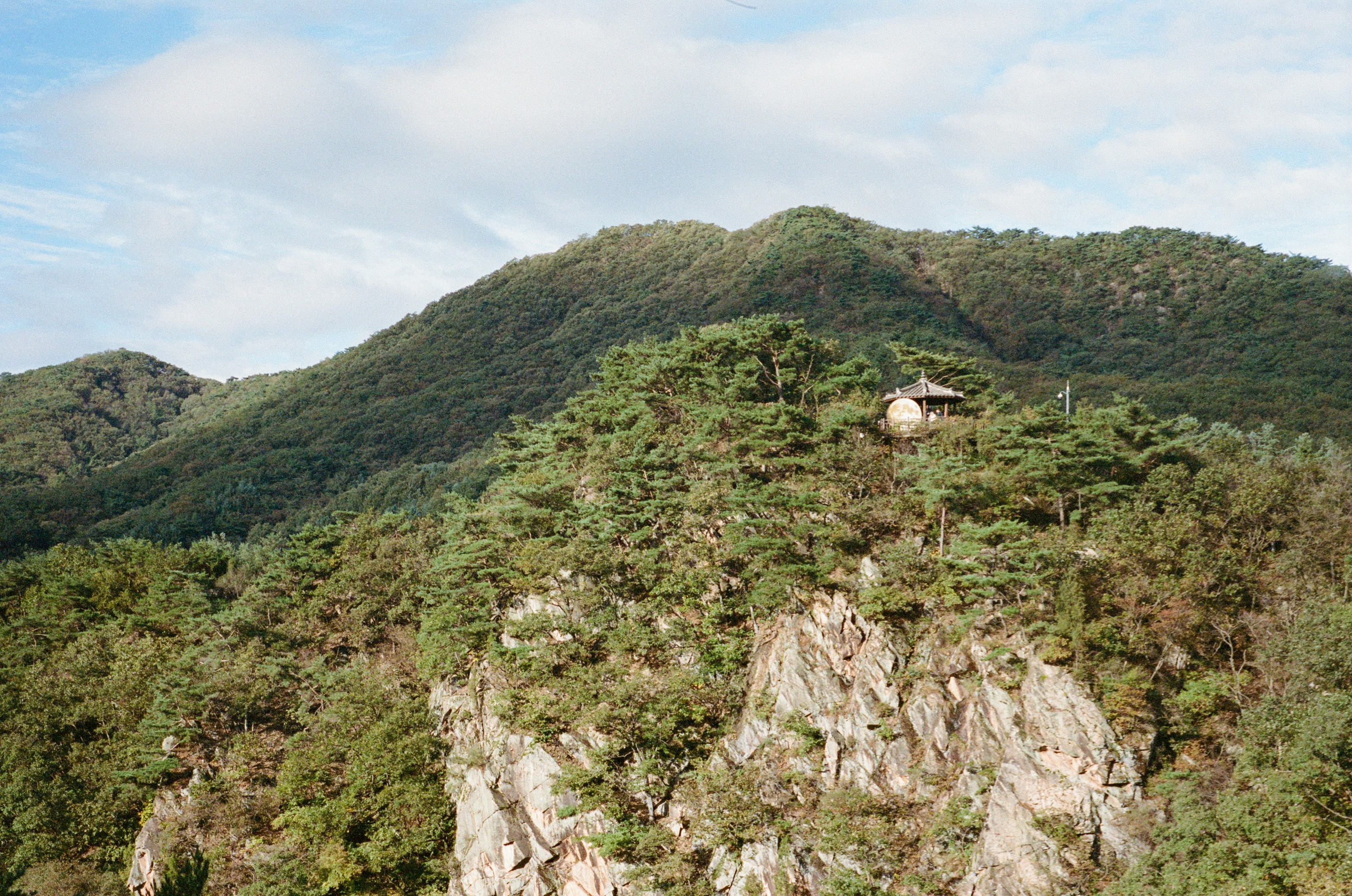 小さな建物が岩だらけで木々に覆われた山の頂上に建っています。