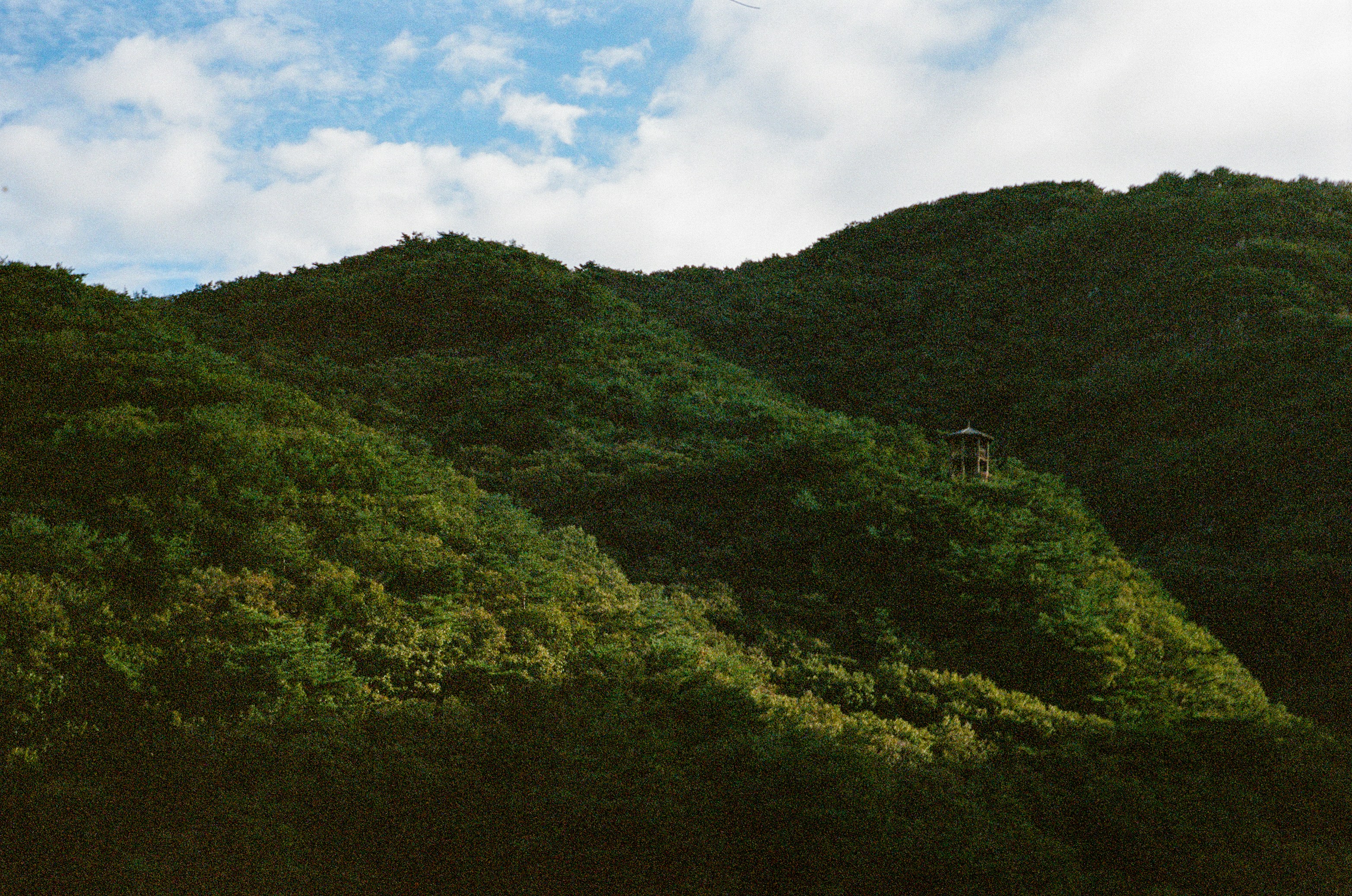 緑豊かな山々と、頂上に小さな建物がある。