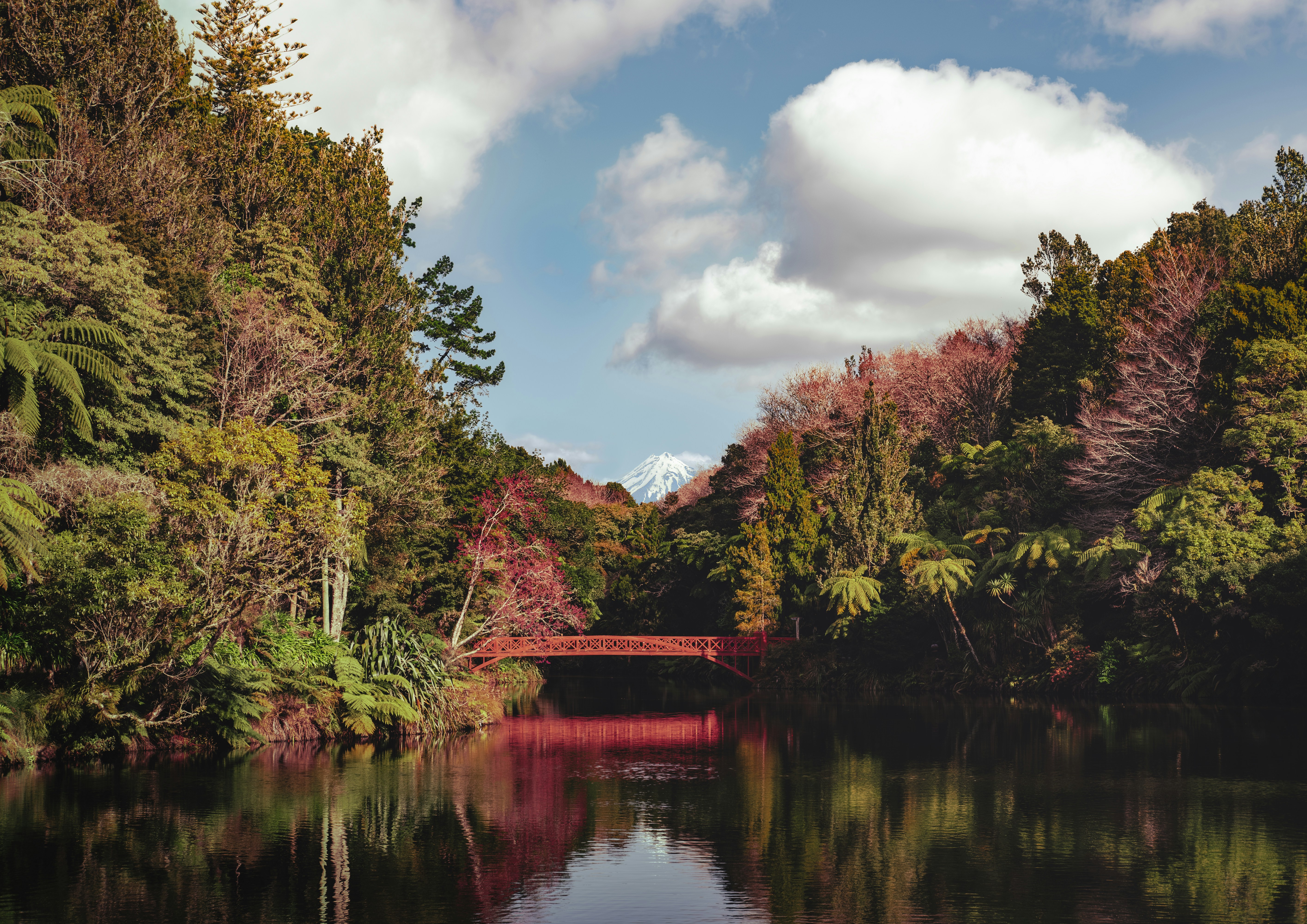 A red bridge over a calm river surrounded by trees.