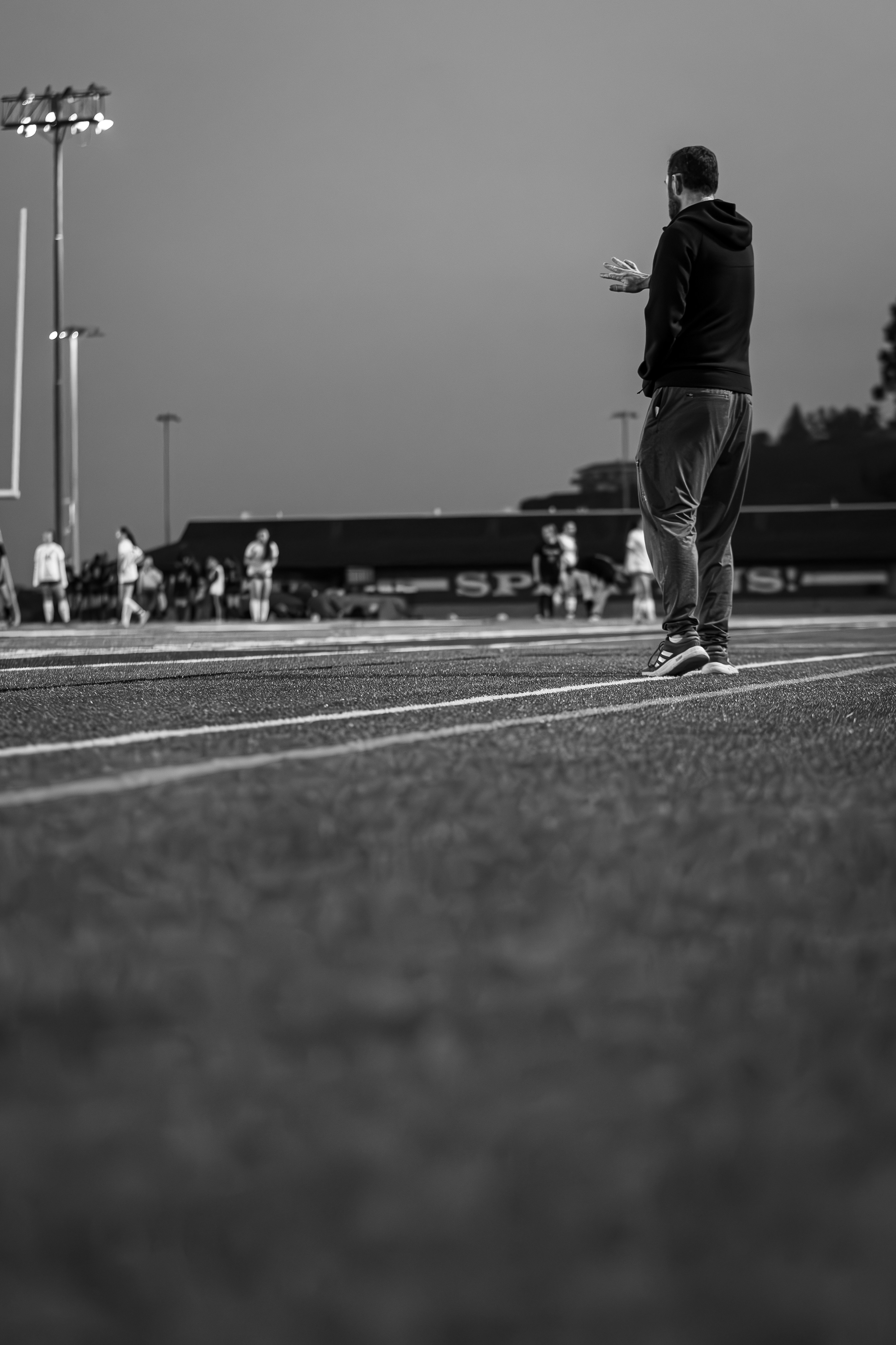 Coach gesturing on a football field at dusk