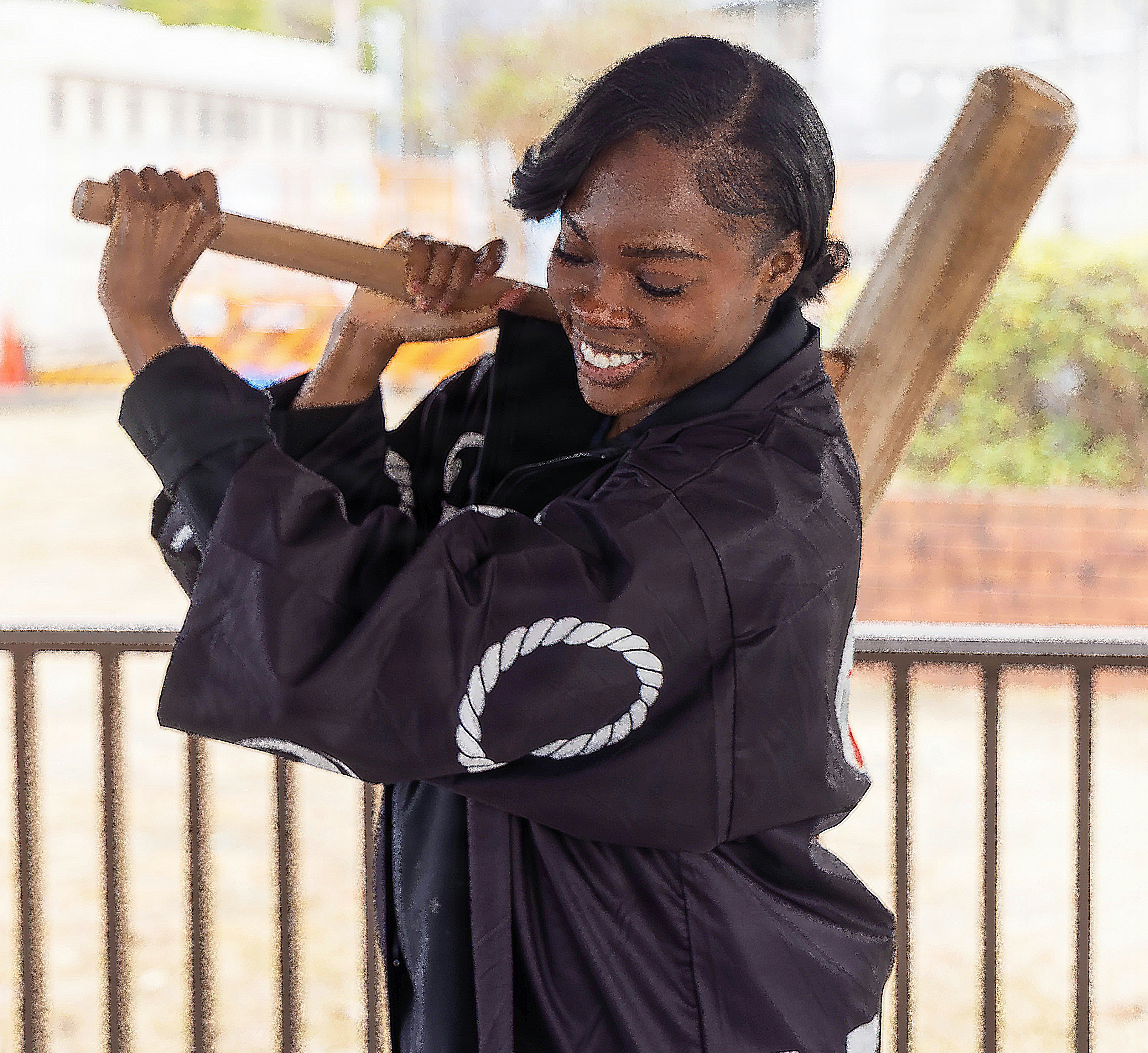 Uma mulher de jaqueta preta balança um taco de madeira.