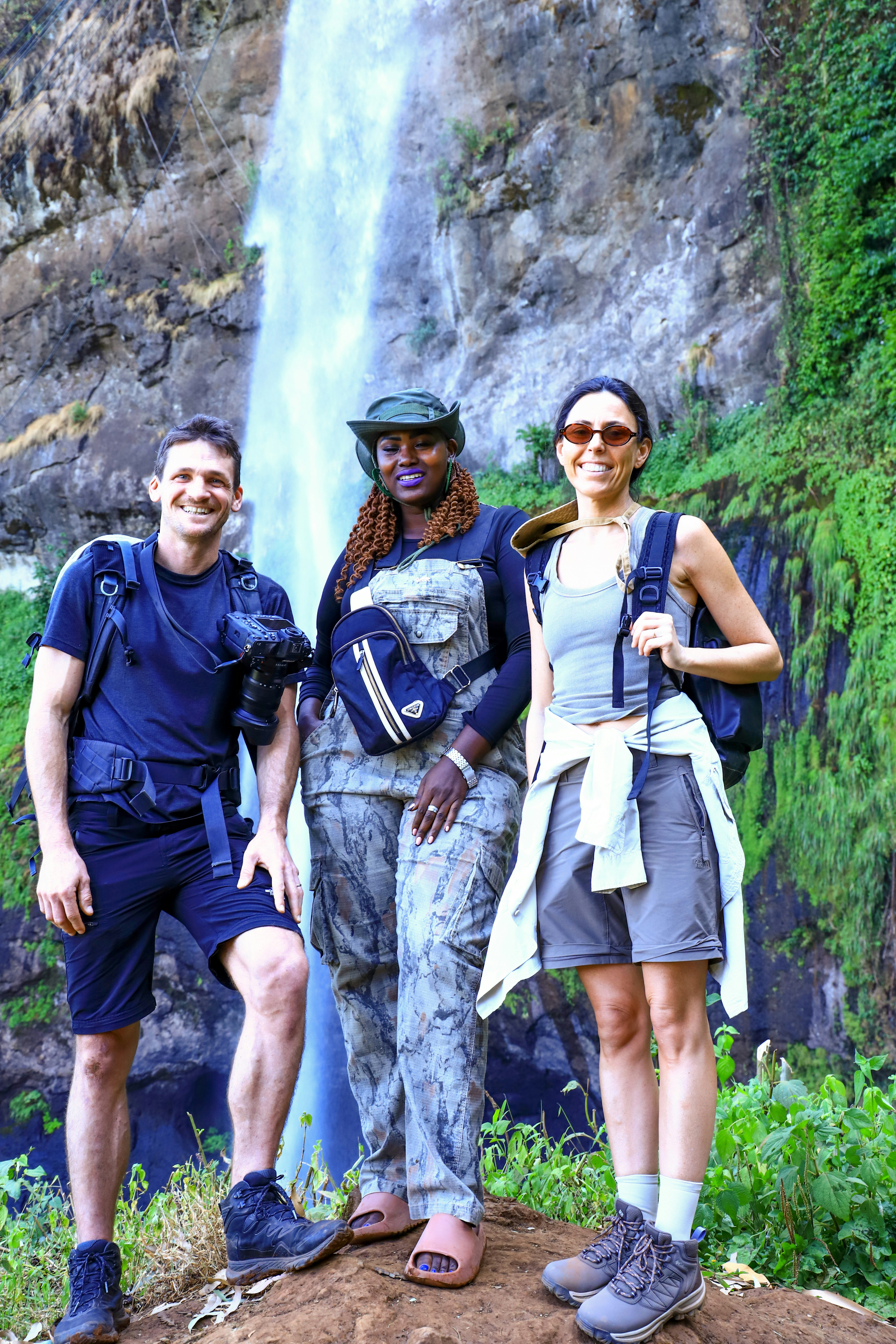 Three hikers pose in front of a waterfall