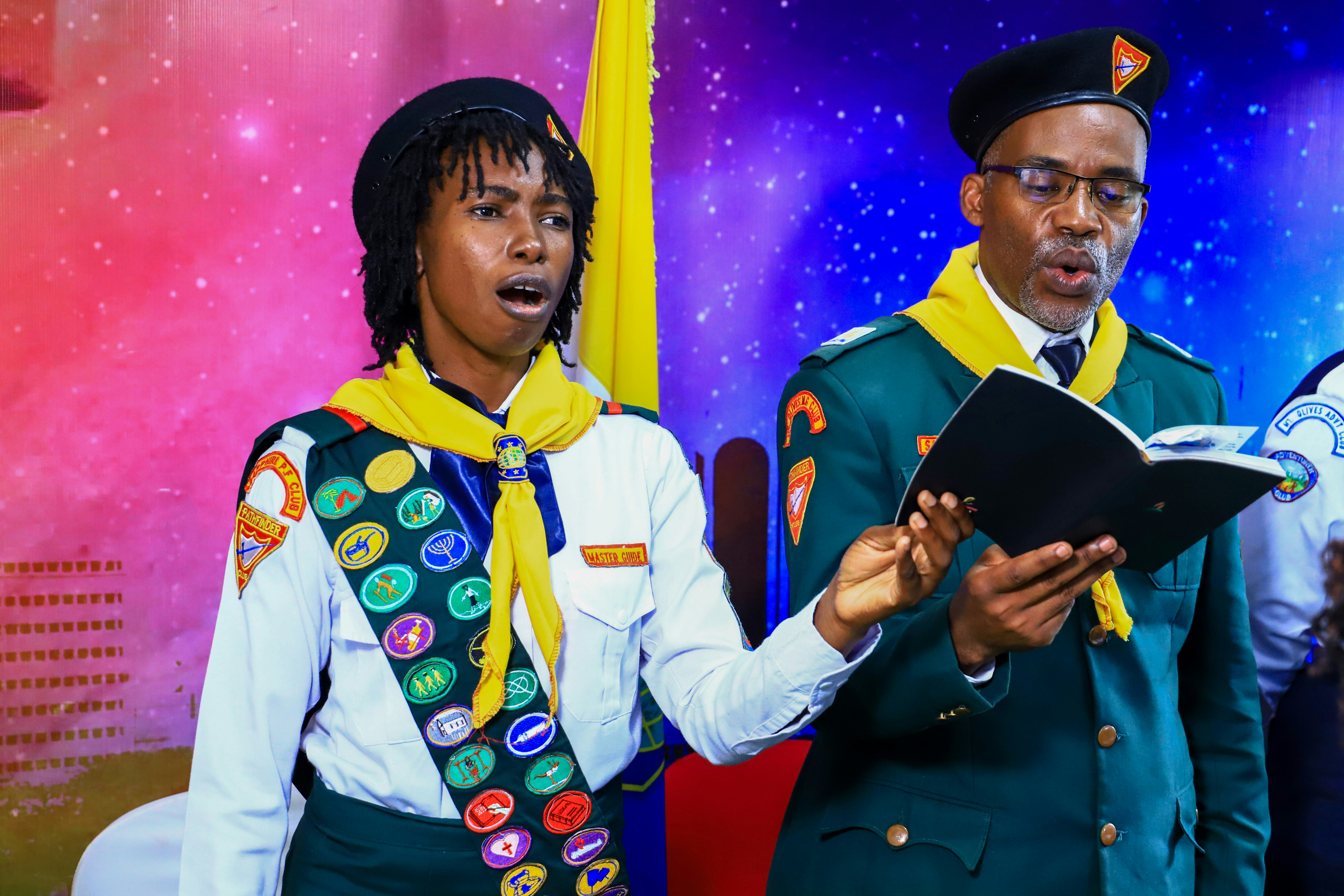 Two people in scout uniforms singing from a book