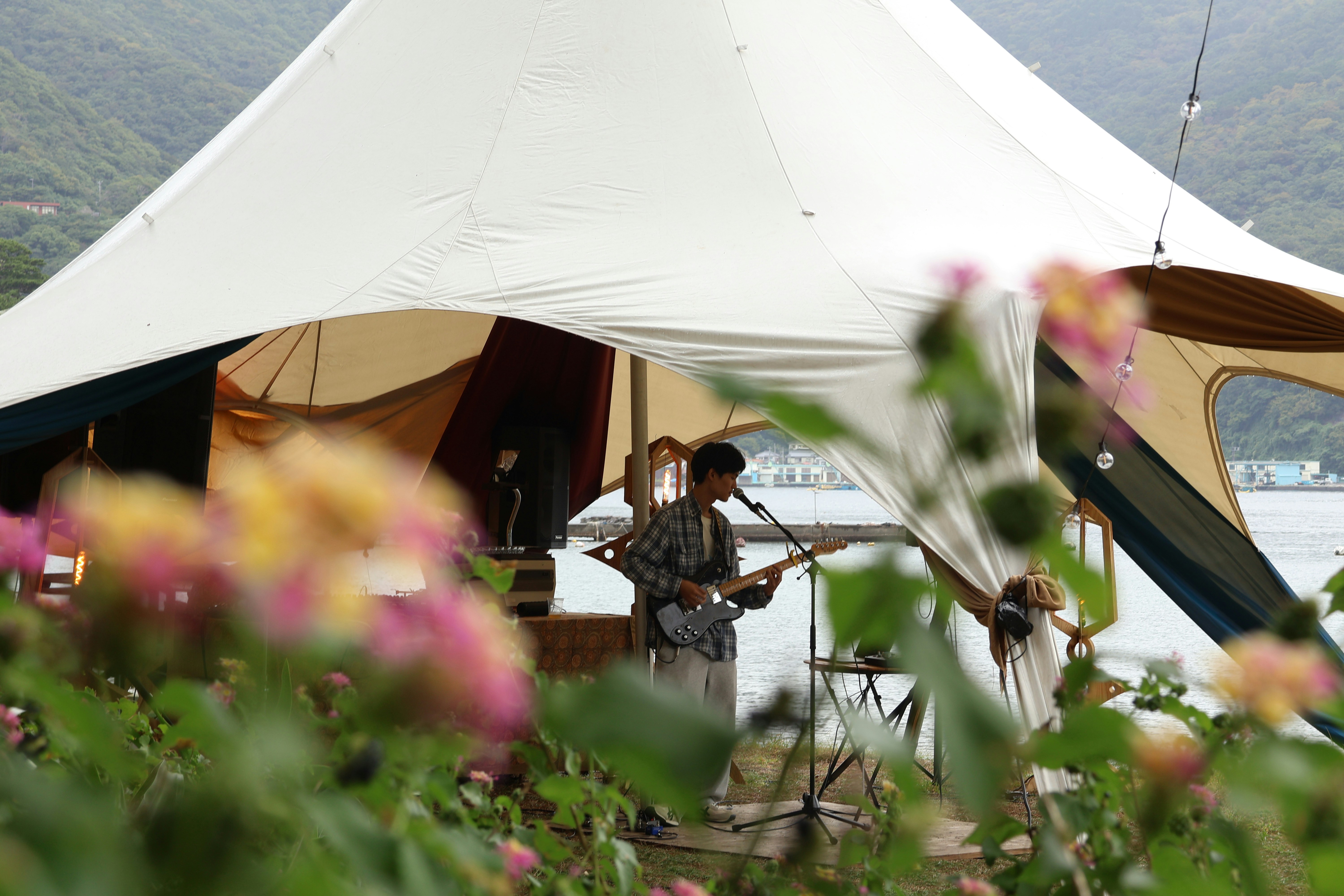 Musicians play under a large tent near water.