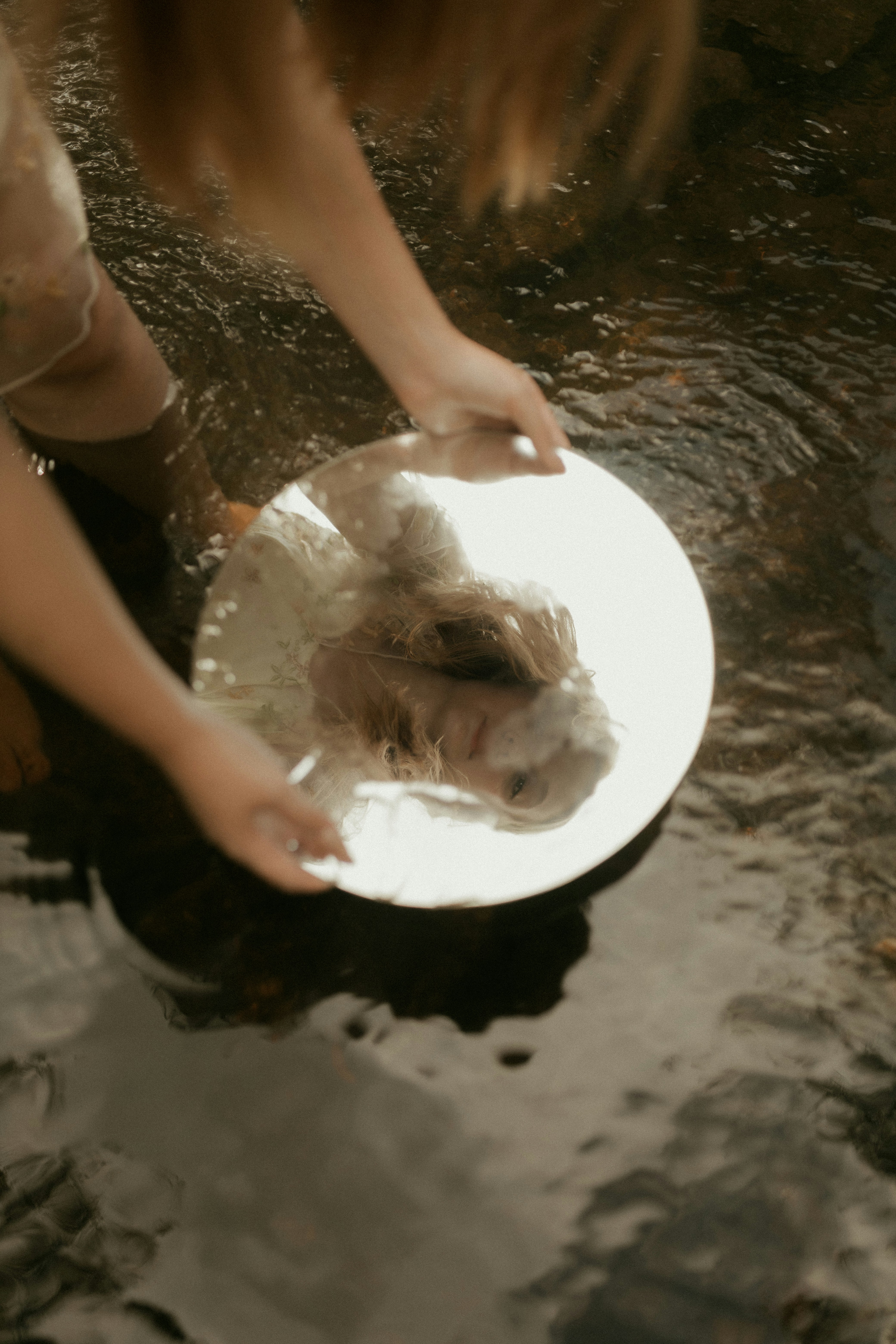 Woman holding a round mirror in shallow water.