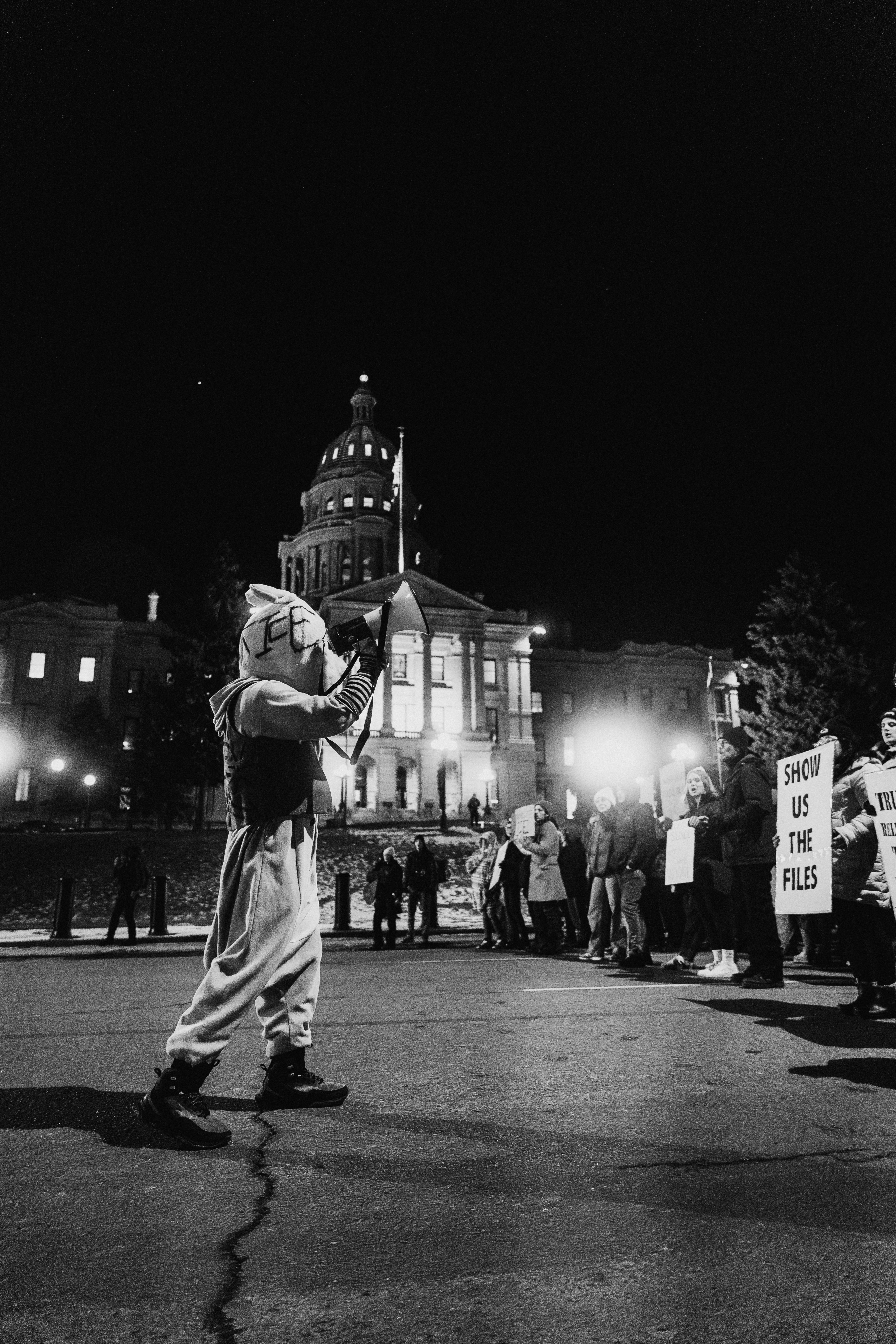 Des manifestants en costume manifestent devant un bâtiment illuminé la nuit