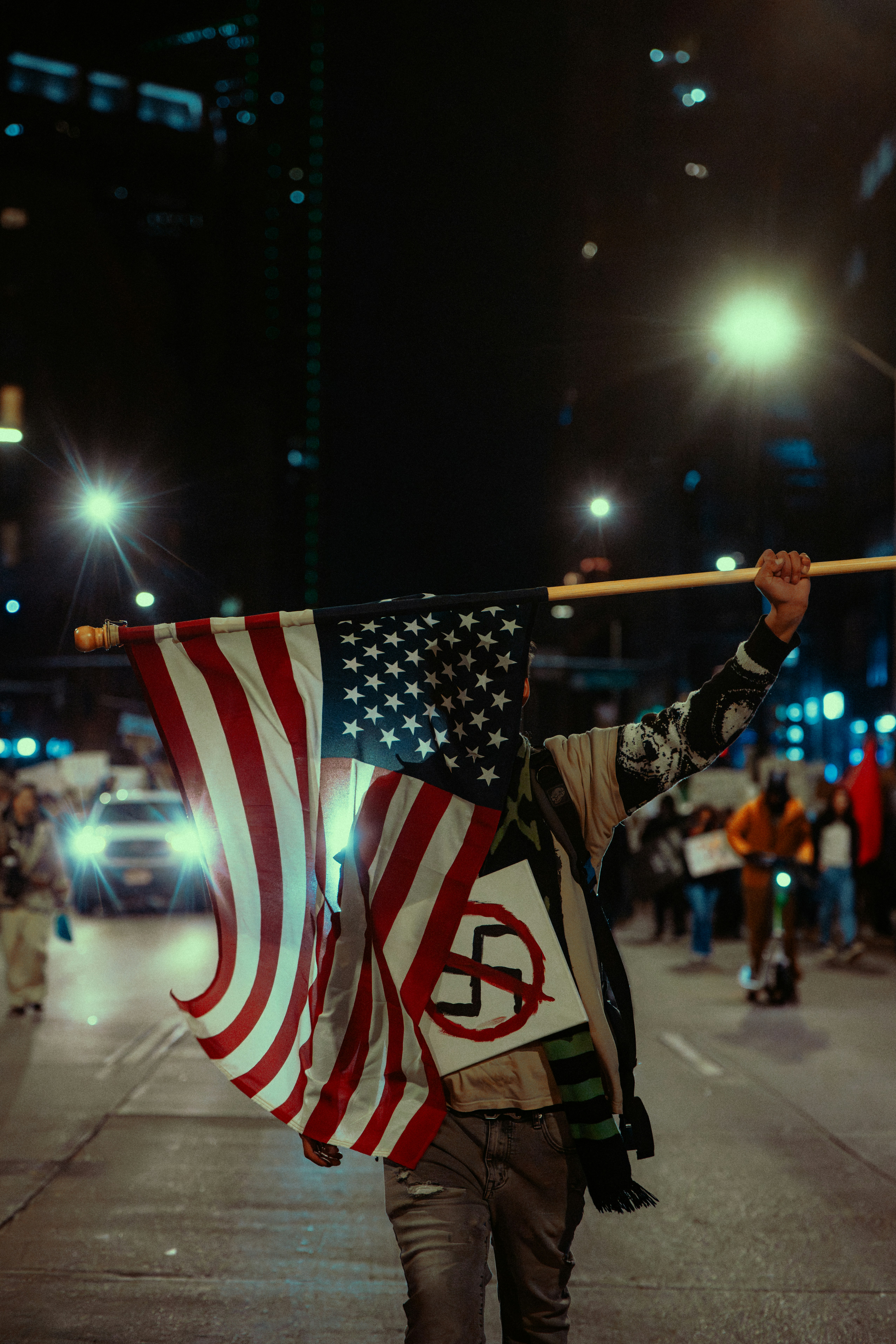 Personne tenant un drapeau américain et un symbole anti-nazi la nuit.