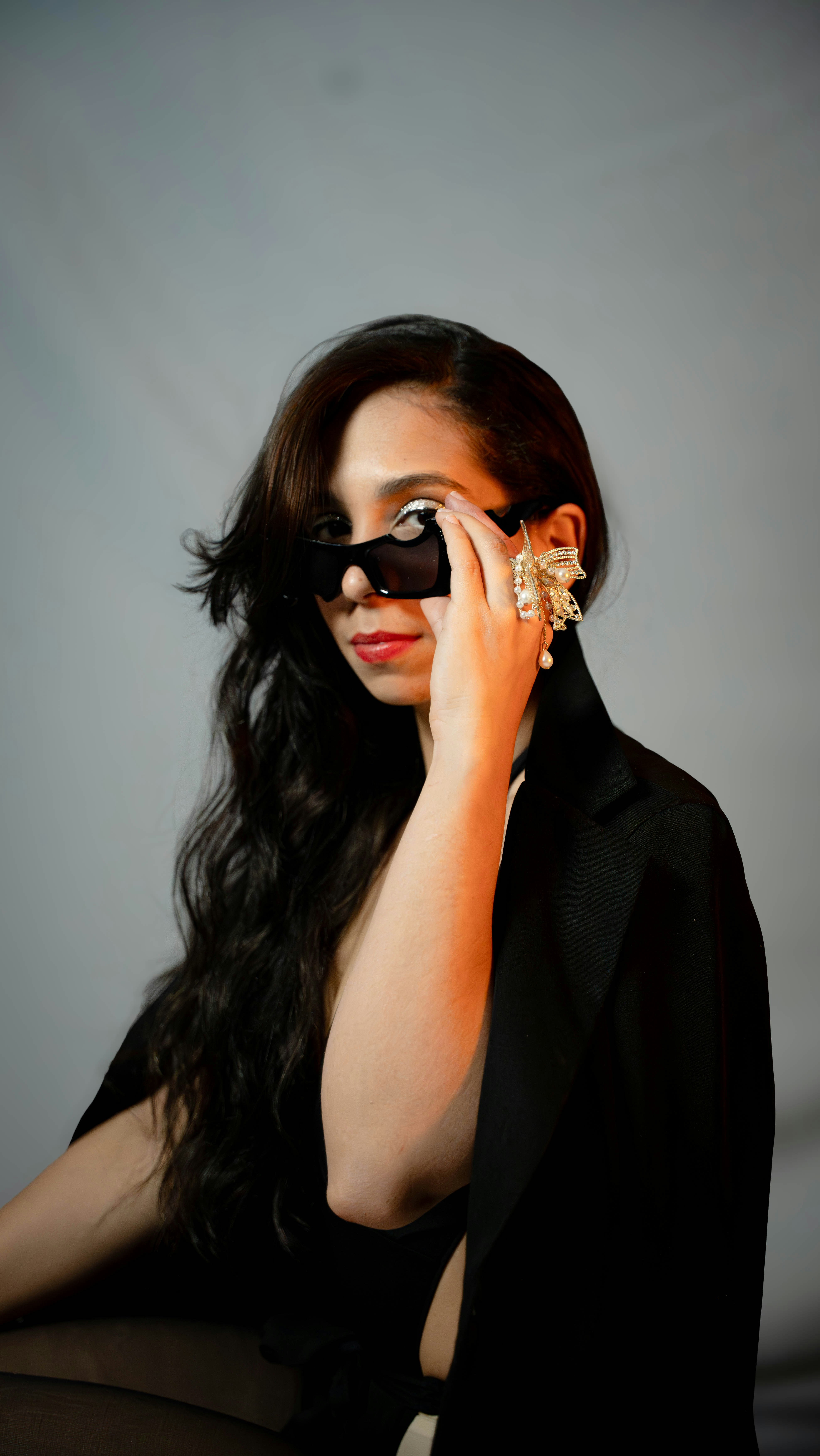 Woman in sunglasses and large earrings with hand on face.