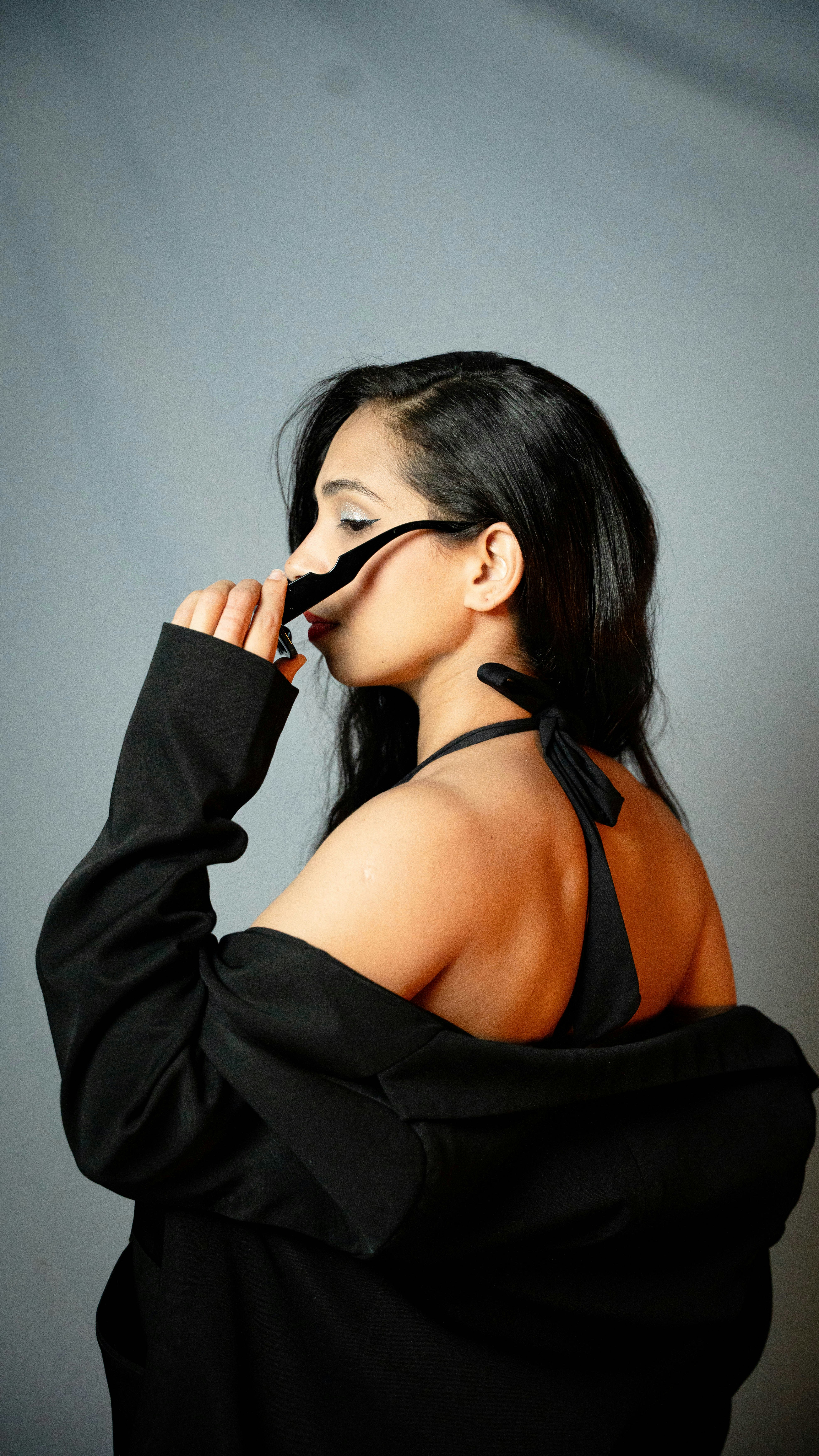 Woman in black jacket and bikini top adjusts sunglasses