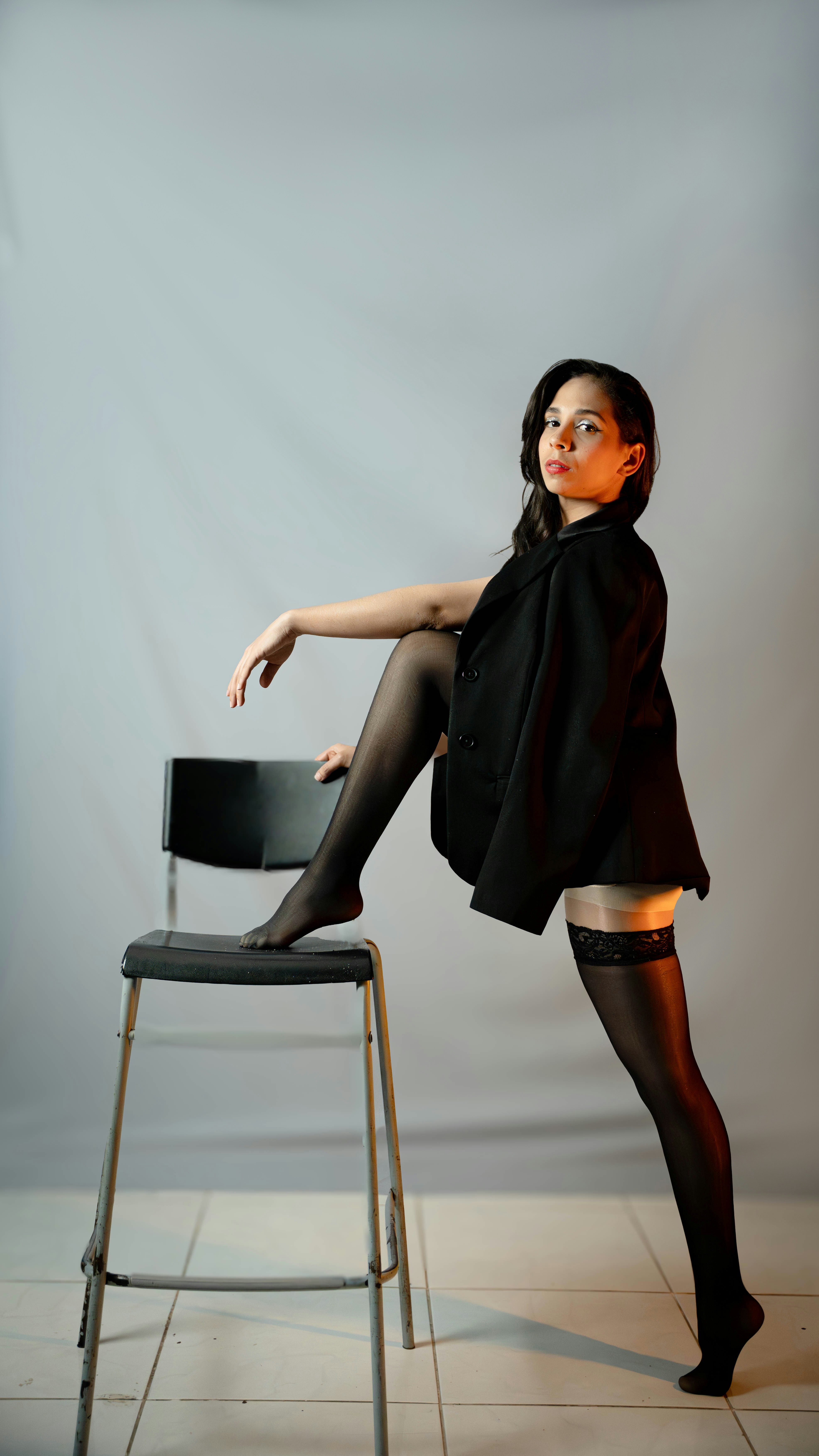 Woman in black blazer and stockings on stool.
