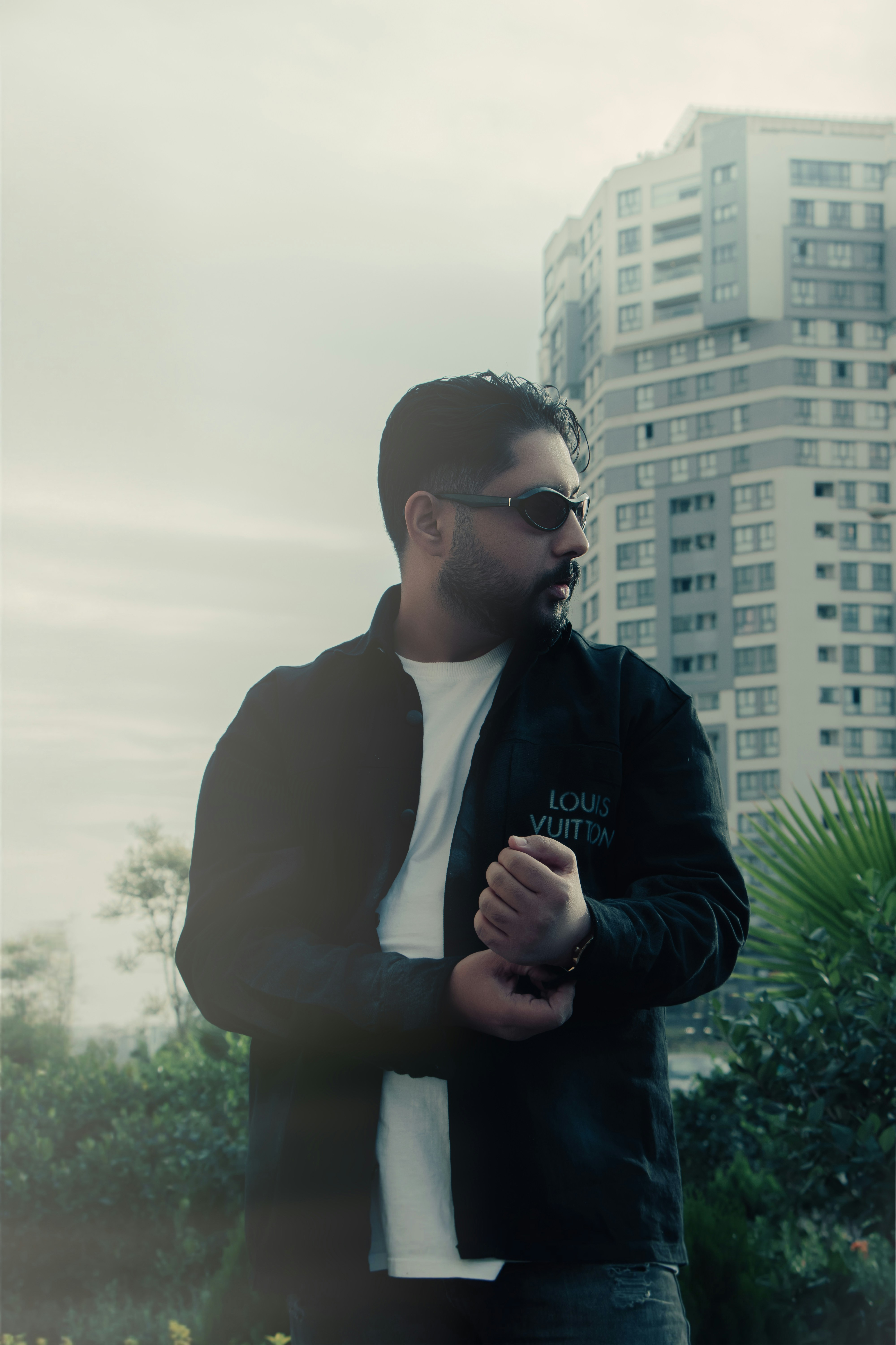Man in sunglasses adjusts cuff in front of tall building.
