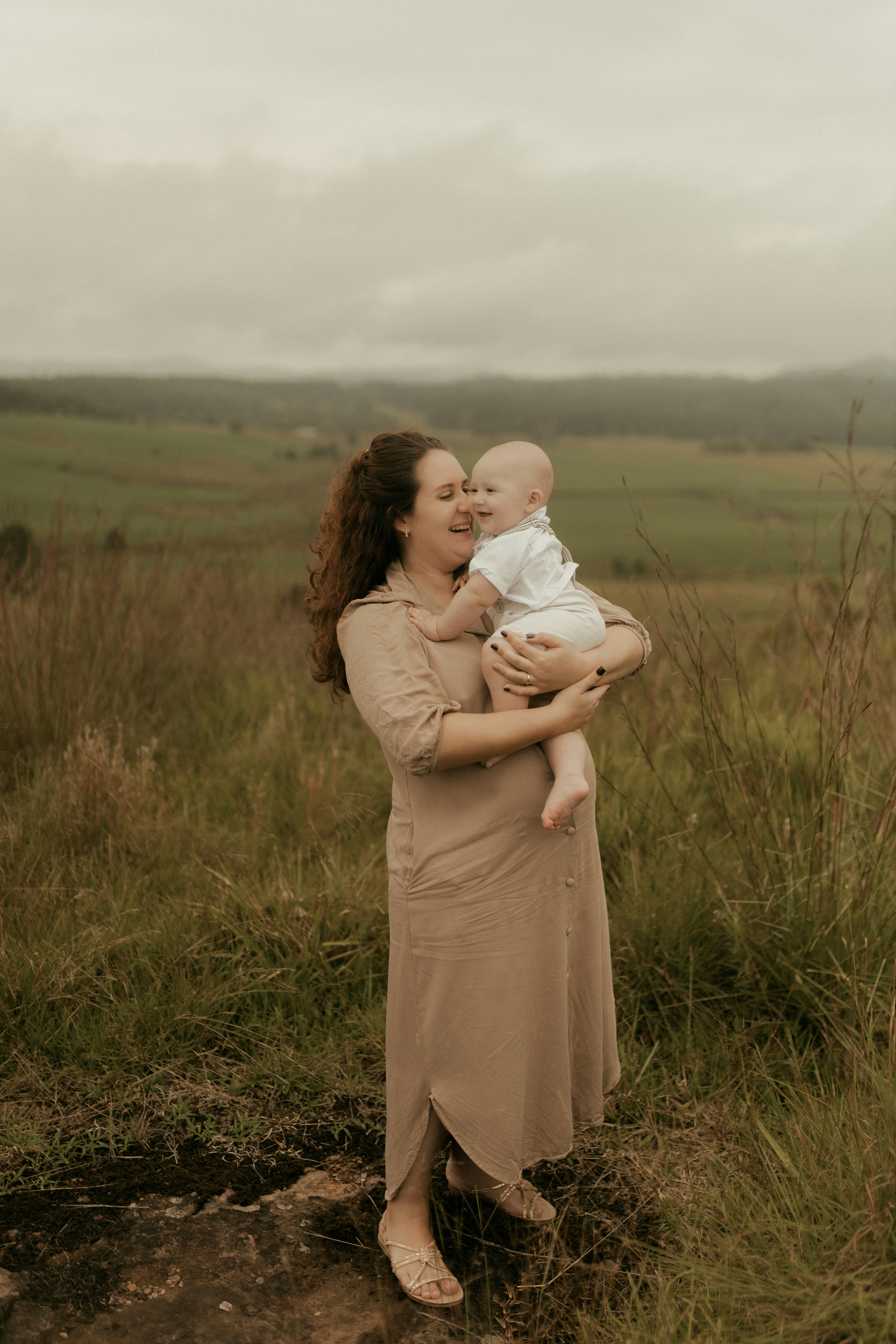 Eine Mutter hält ihr lächelndes Baby auf einer Graswiese.